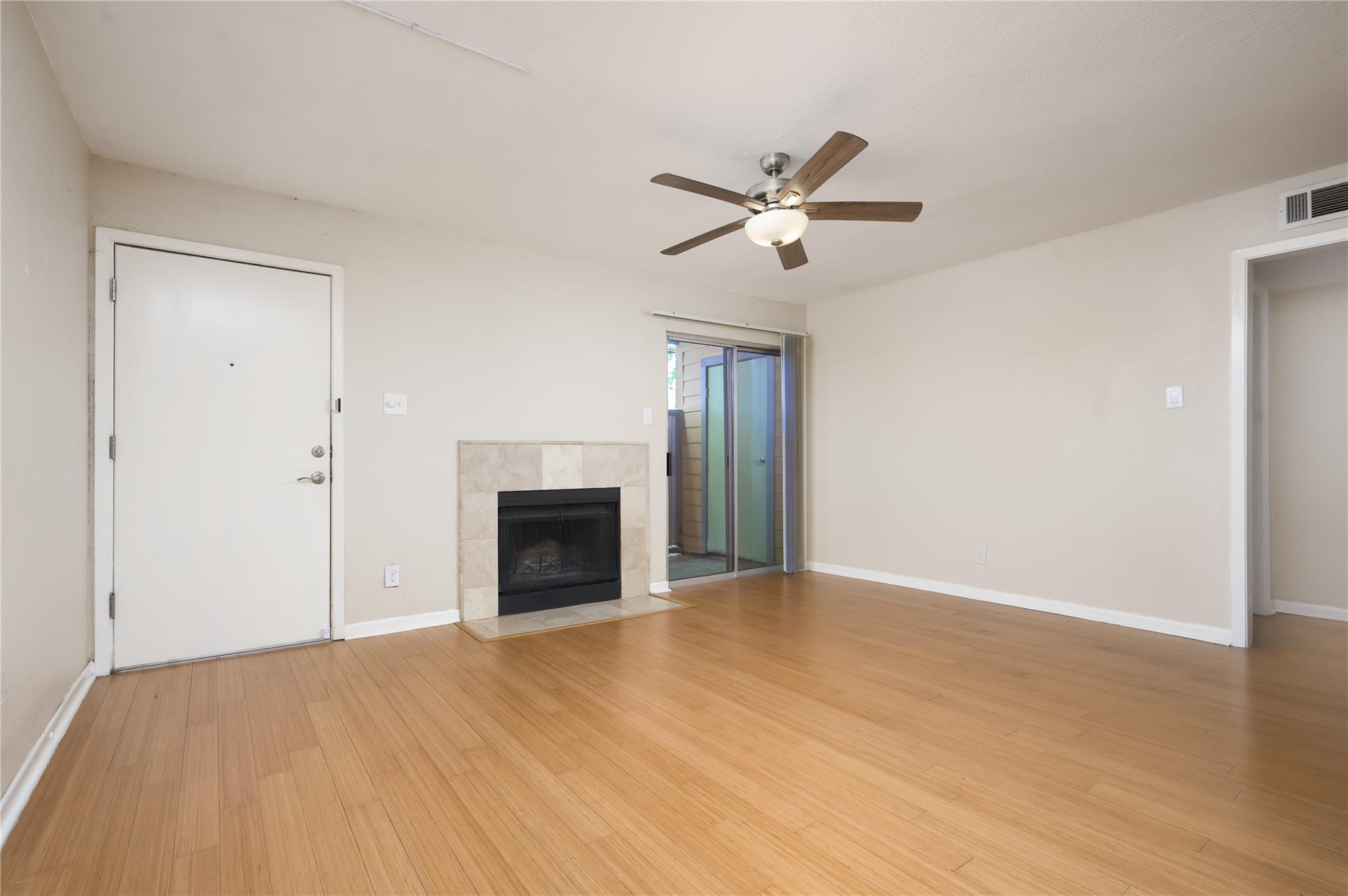 Empty living room with wood flooring, tiled fireplace, and sliding glass door.