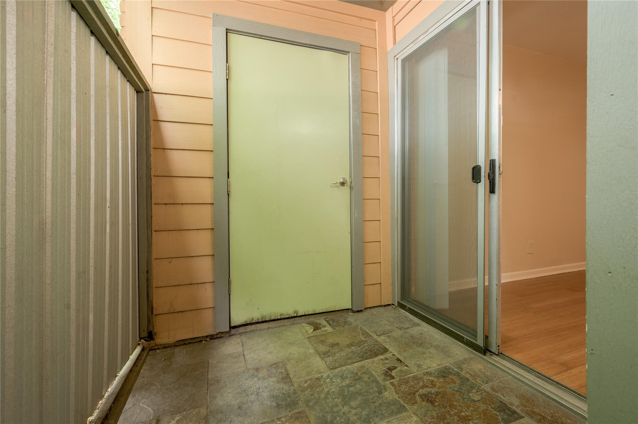Covered entry patio with stone-look tile, a pale green door, and sliding glass doors.