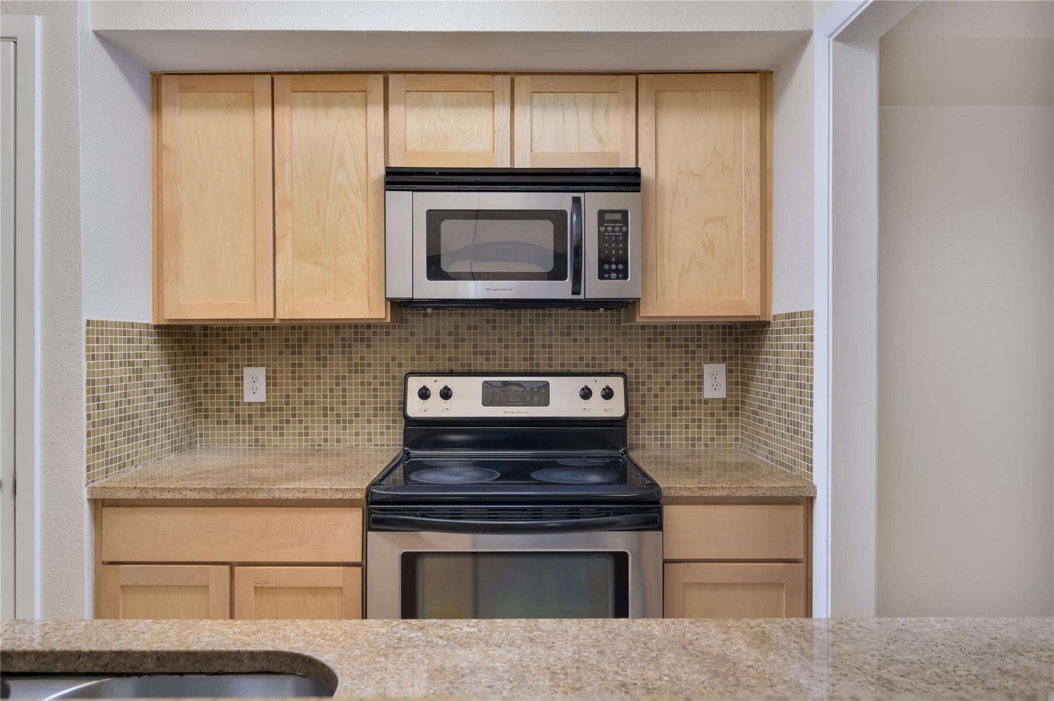 Kitchen with light wood cabinets, mosaic tile backsplash, and stainless appliances.