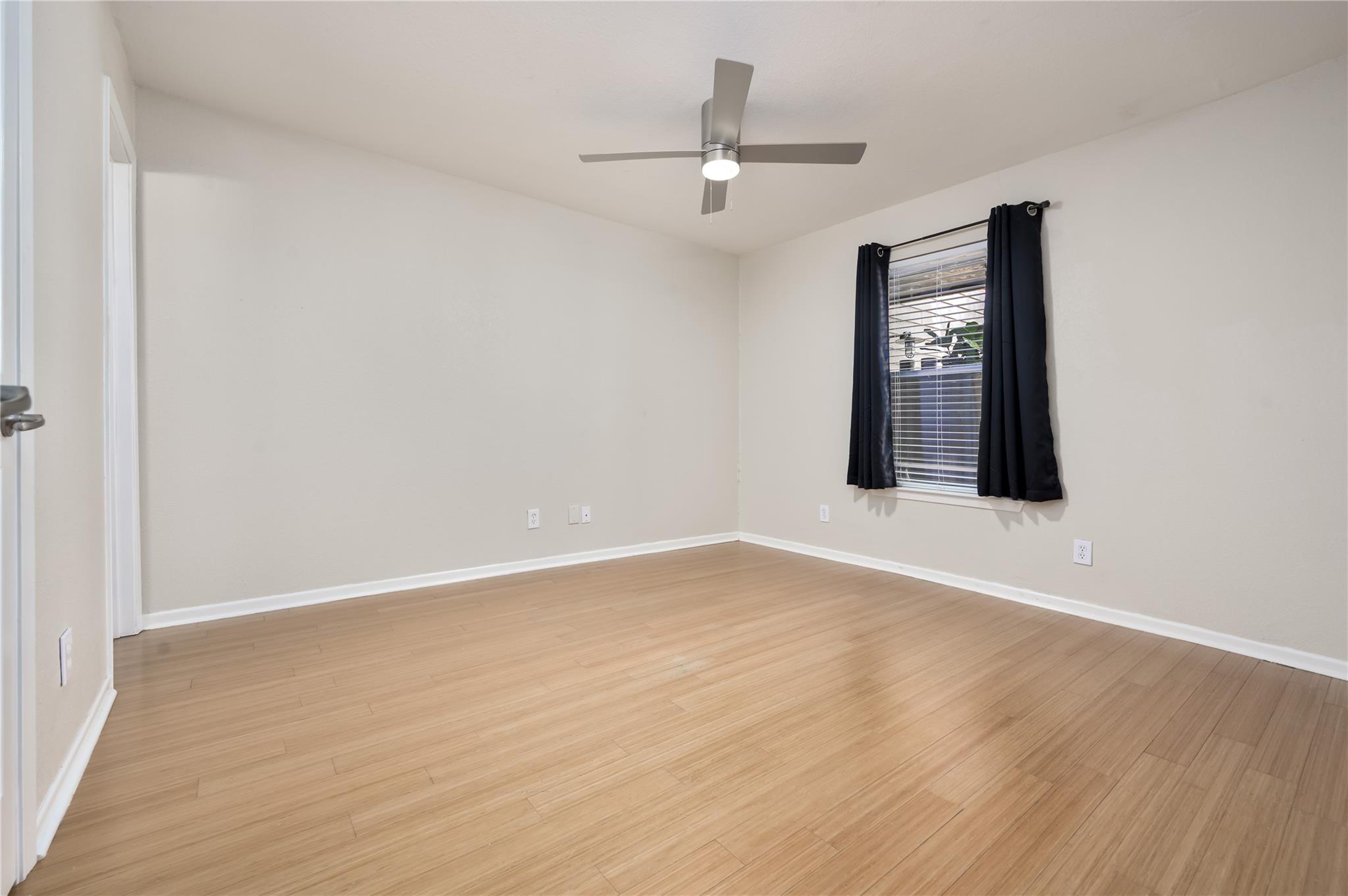 Empty bedroom with light wood-look floors, dark window curtains, and a ceiling fan.