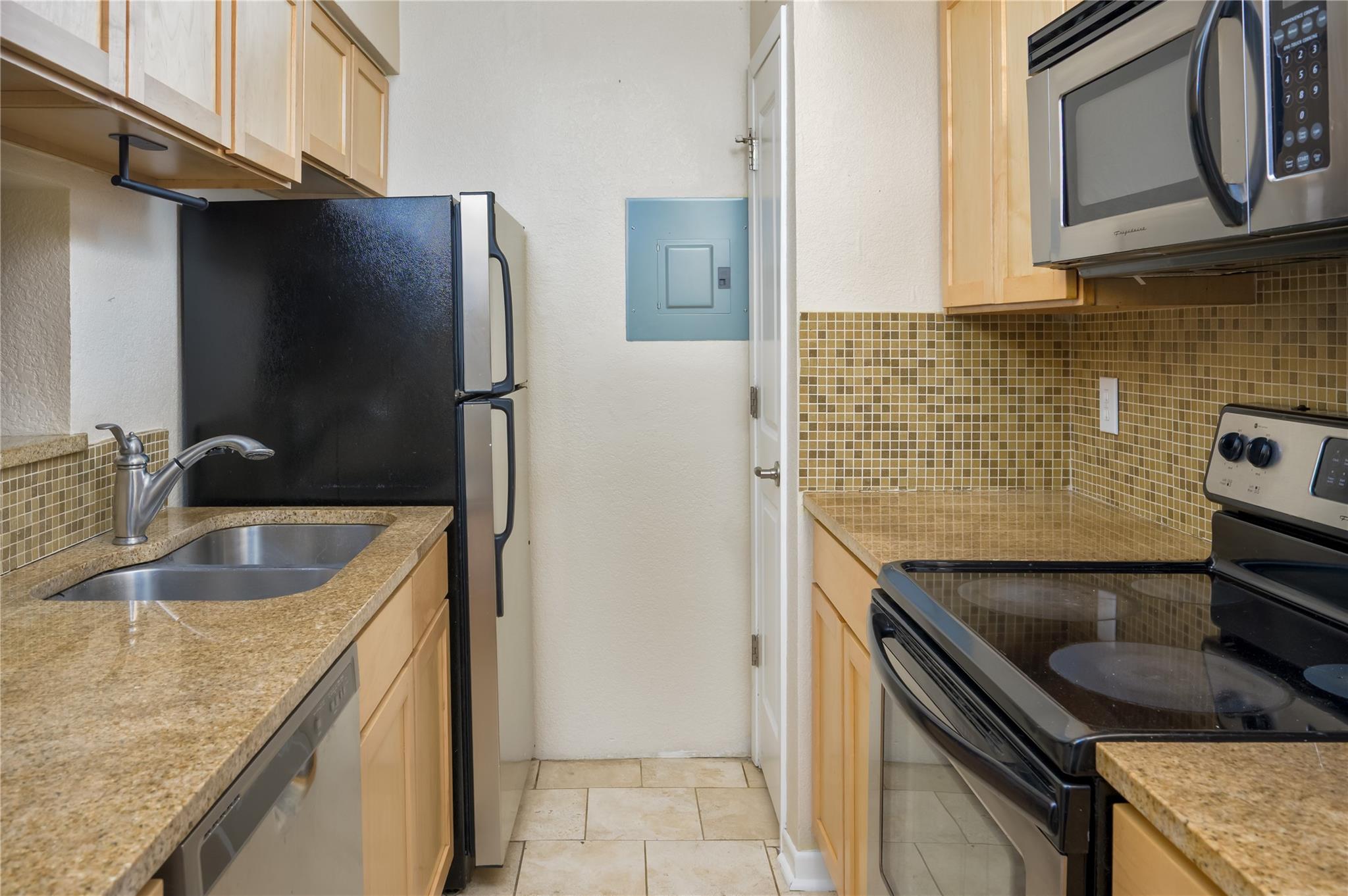 Galley kitchen with granite counters, light wood cabinets, tan tile backsplash, and black appliances.