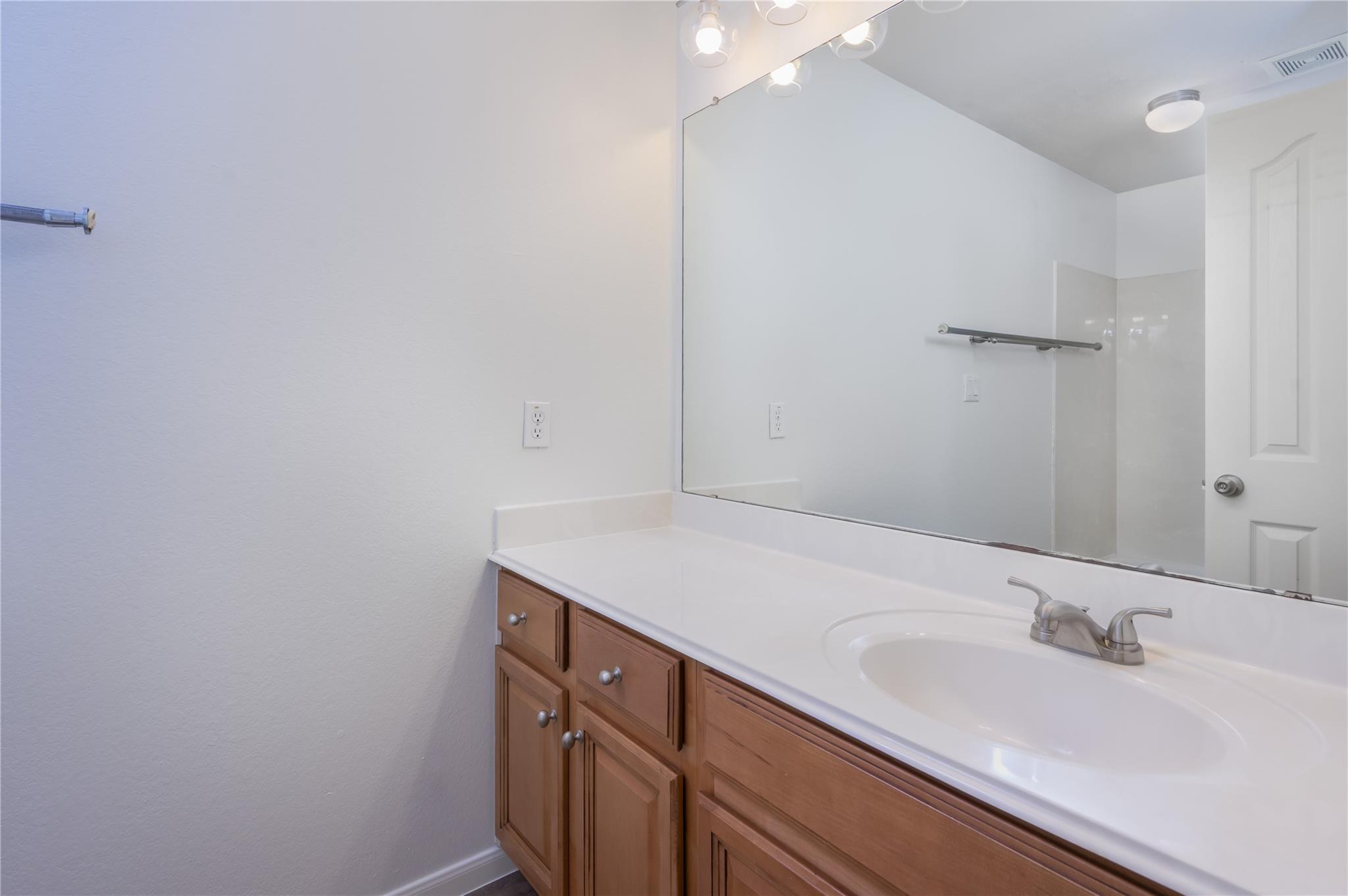 Bathroom vanity with a wide mirror, white countertop, oval sink, and wood cabinetry.
