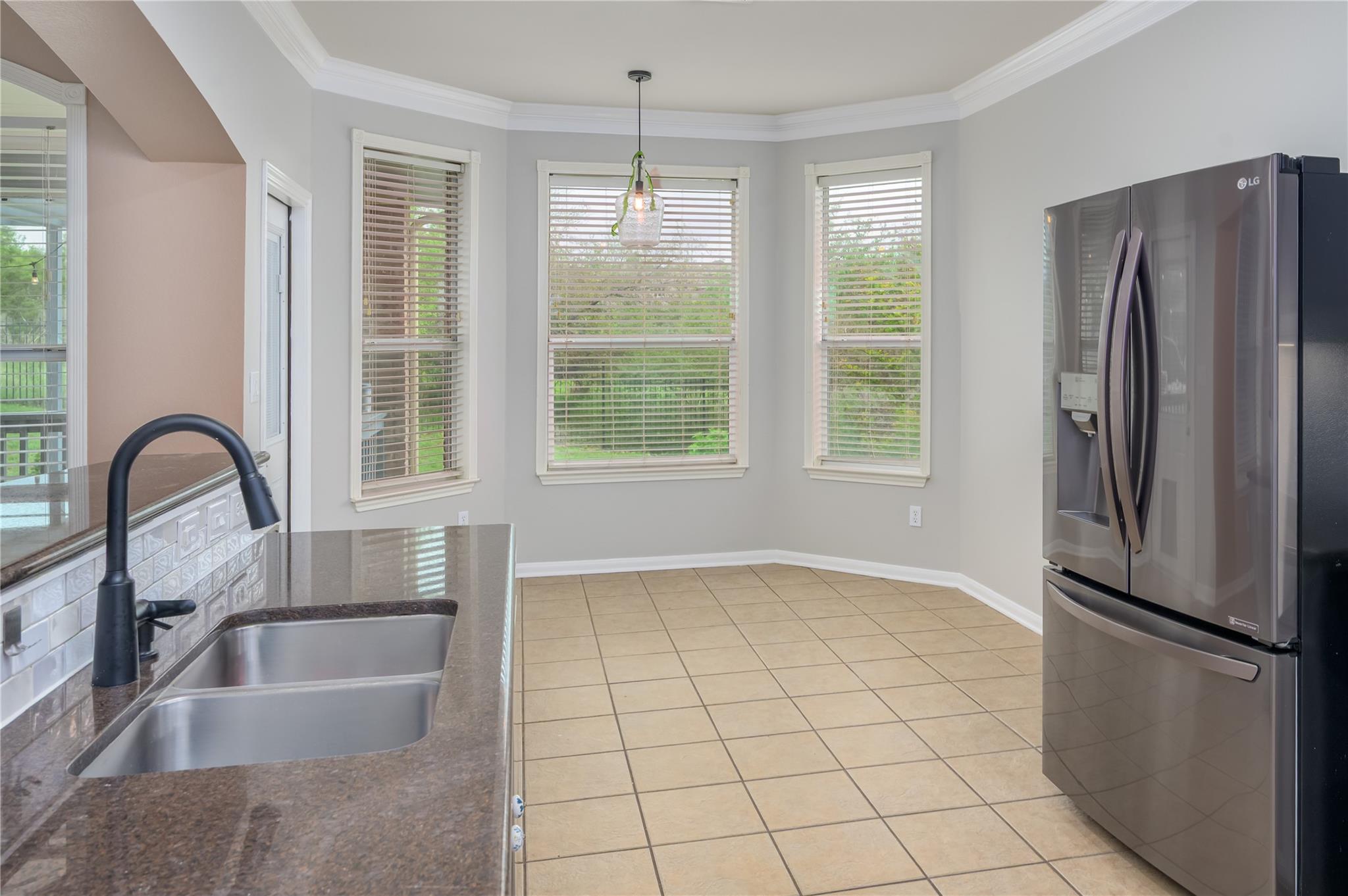 Kitchen with a double-basin sink, stainless refrigerator, and three large windows.