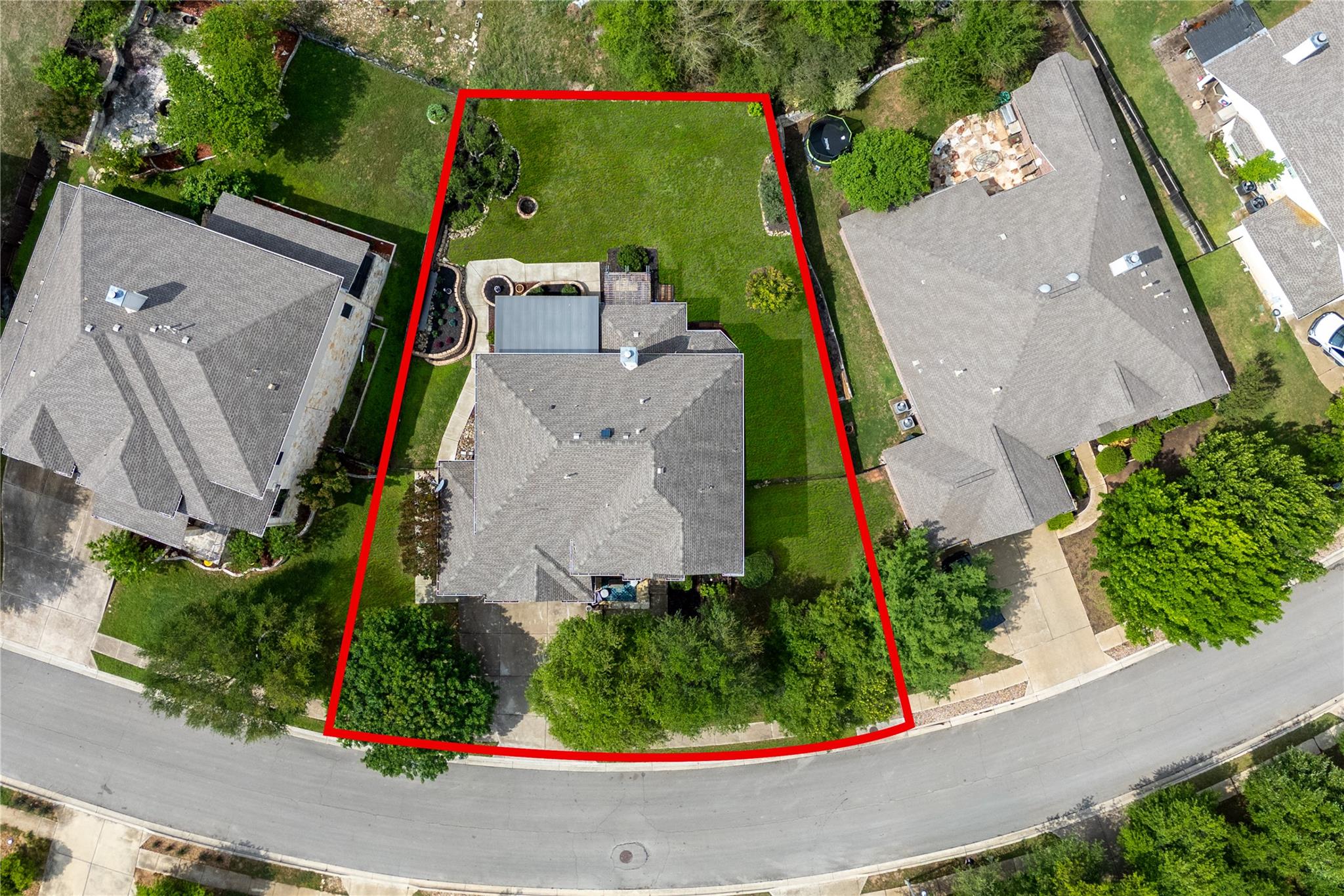 Aerial view of the home and landscaped lot outlined in red, with neighboring houses along the street.