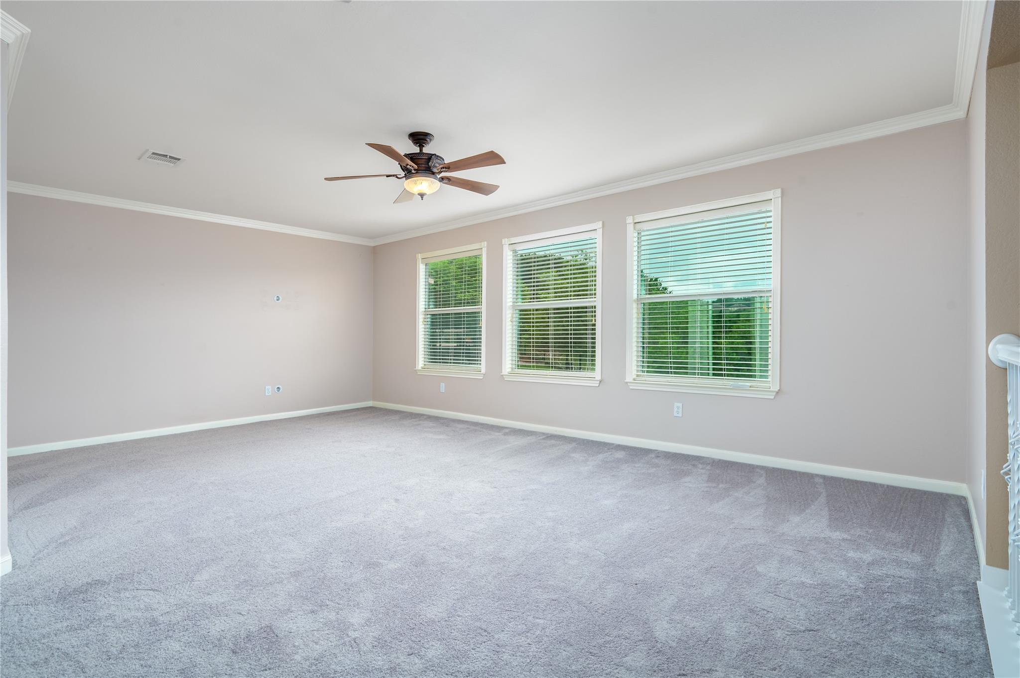 Empty carpeted room with three windows and a ceiling fan.
