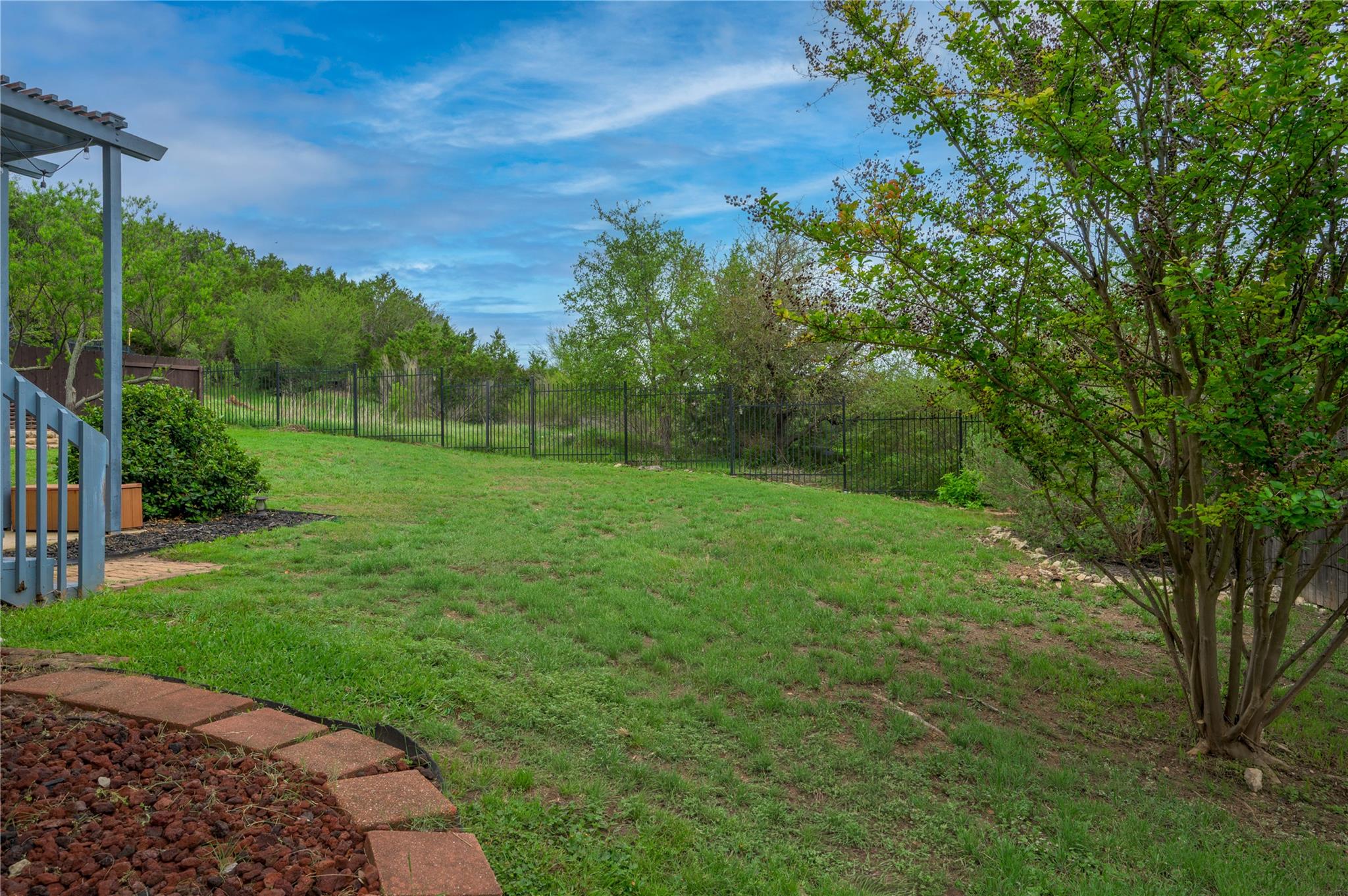 Grassy backyard bordered by a black metal fence, with a covered patio at the edge.