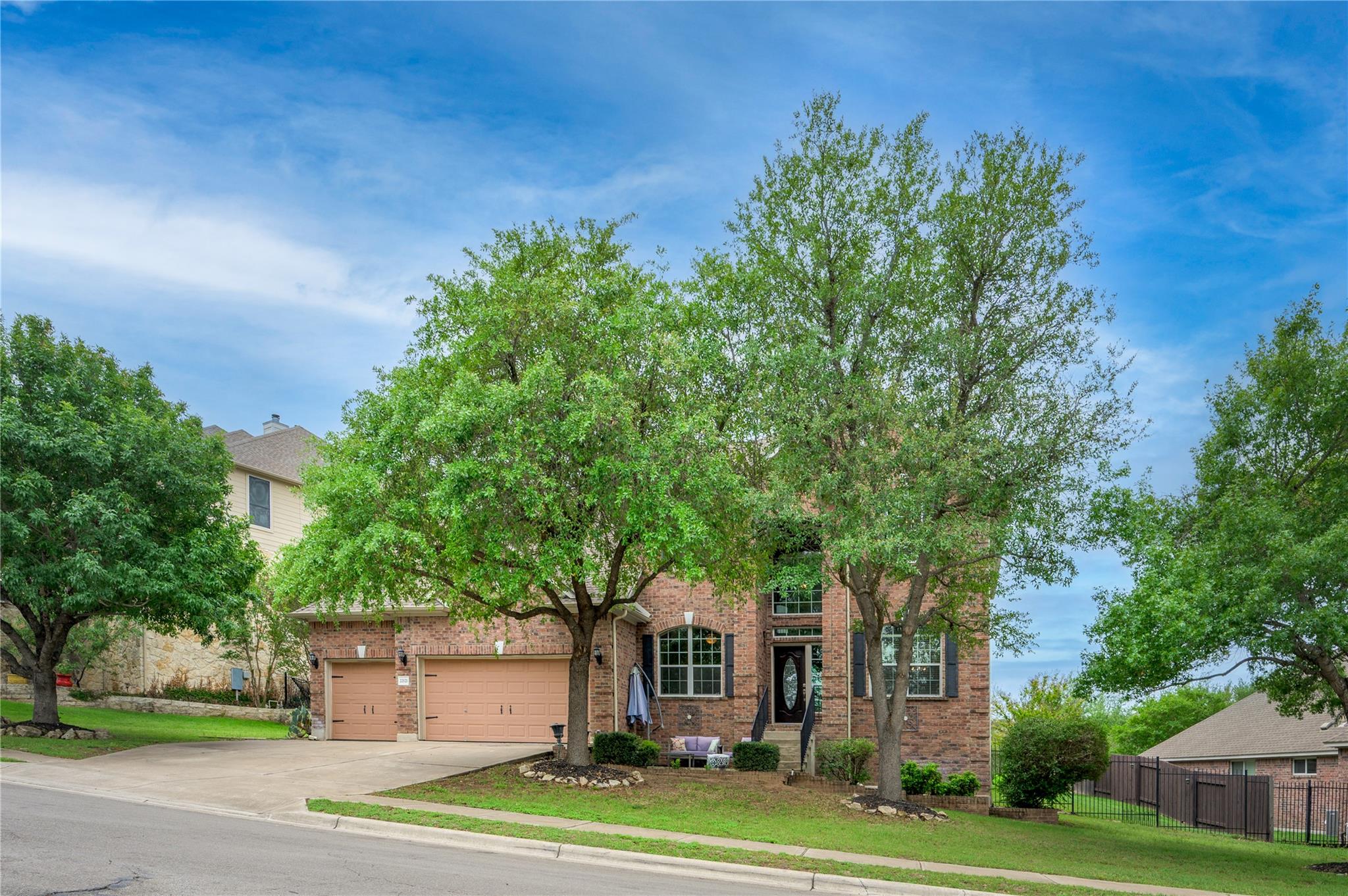 Two-story brick home with a double garage, framed by mature trees.