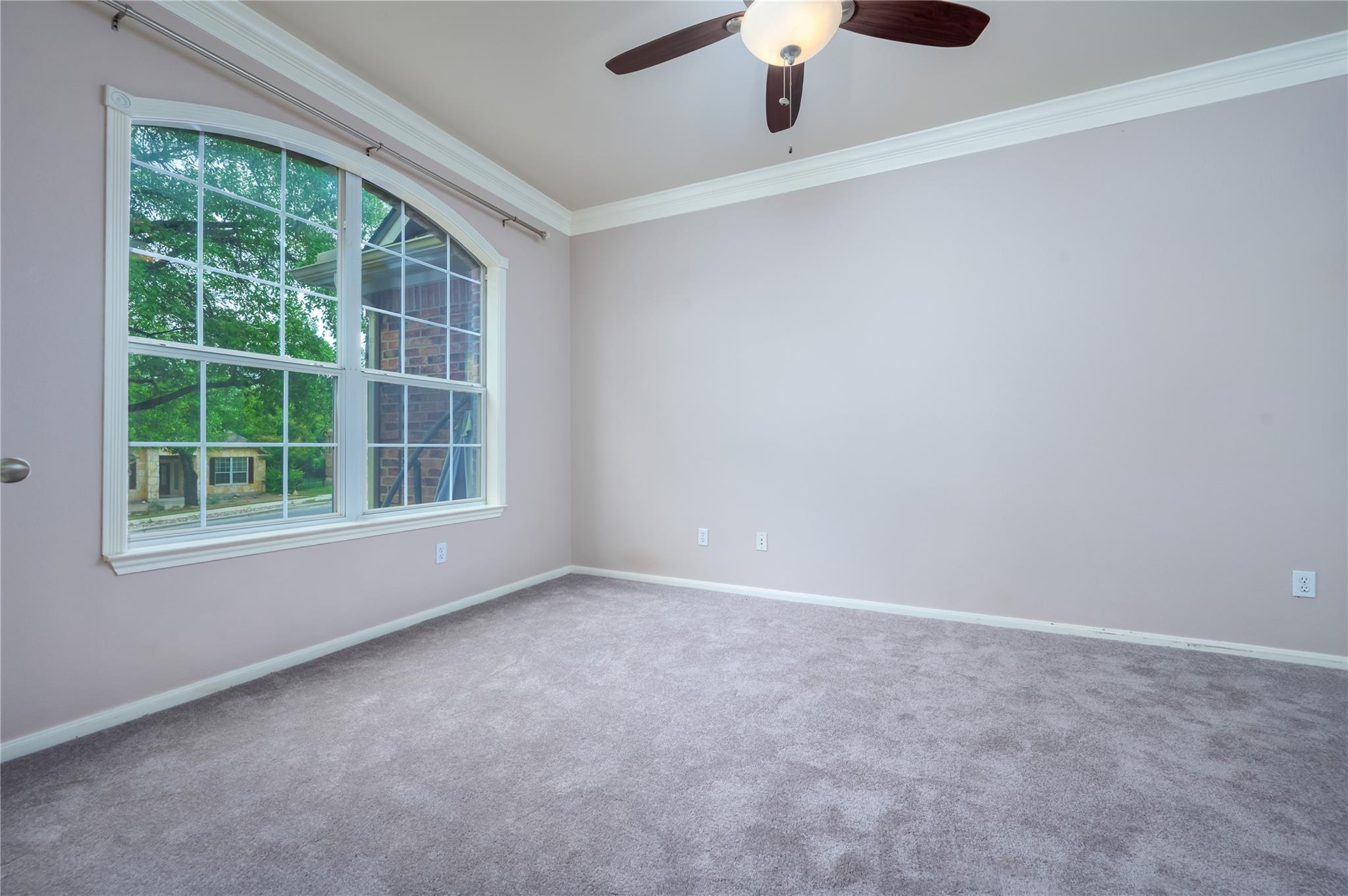 Empty bedroom with gray carpet, a large window, and a ceiling fan.