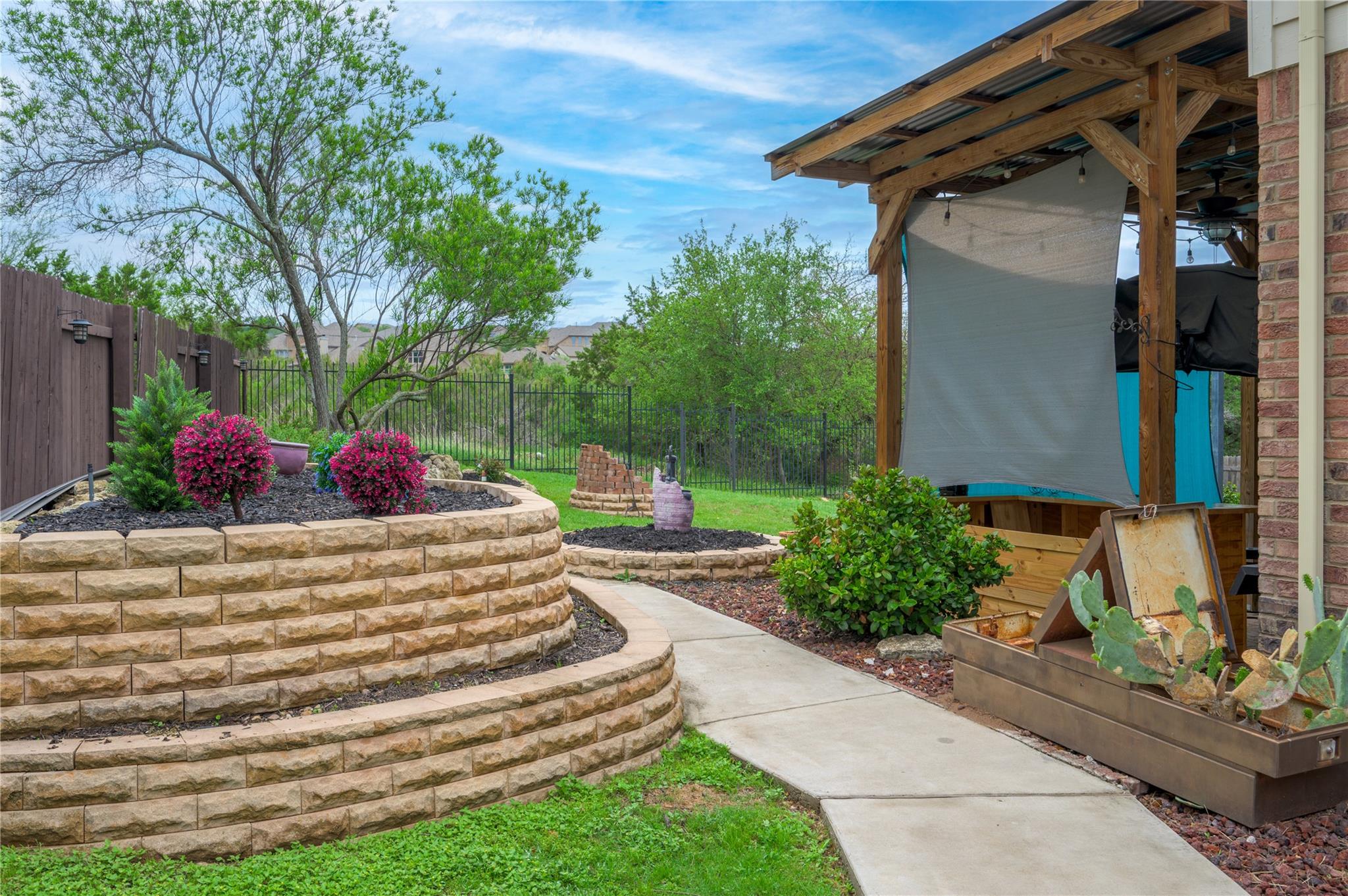 Landscaped backyard with a covered patio, curved stone retaining wall, and flowering shrubs.