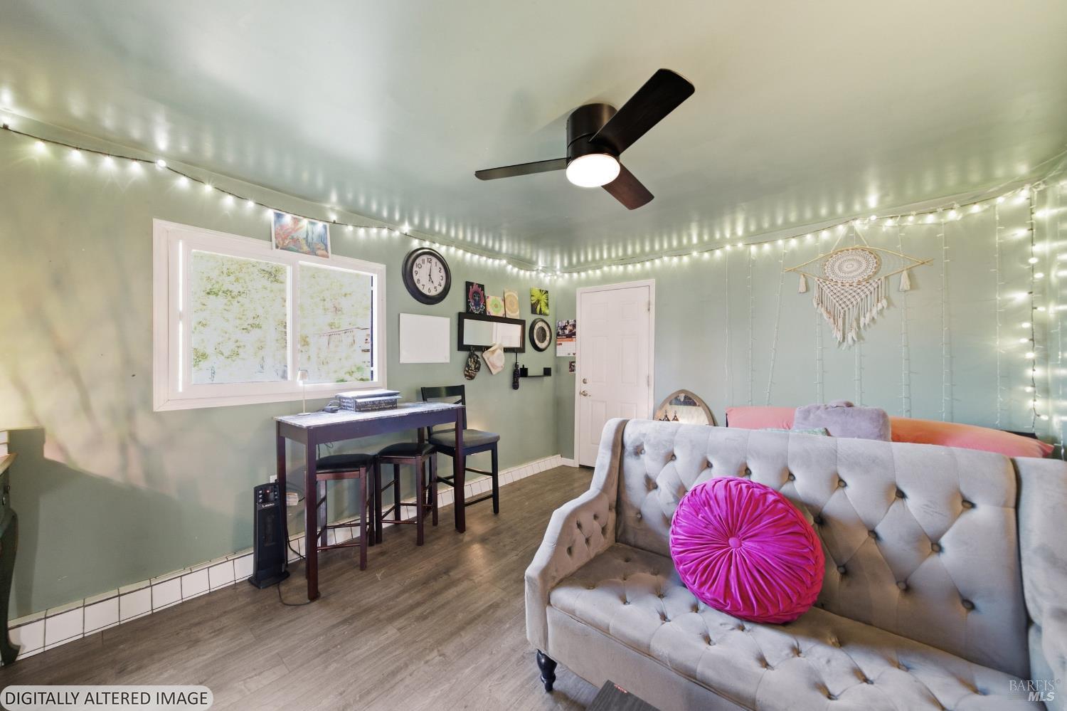 Living room with a tufted gray sofa, pink pillow, ceiling string lights, and desk by the window.