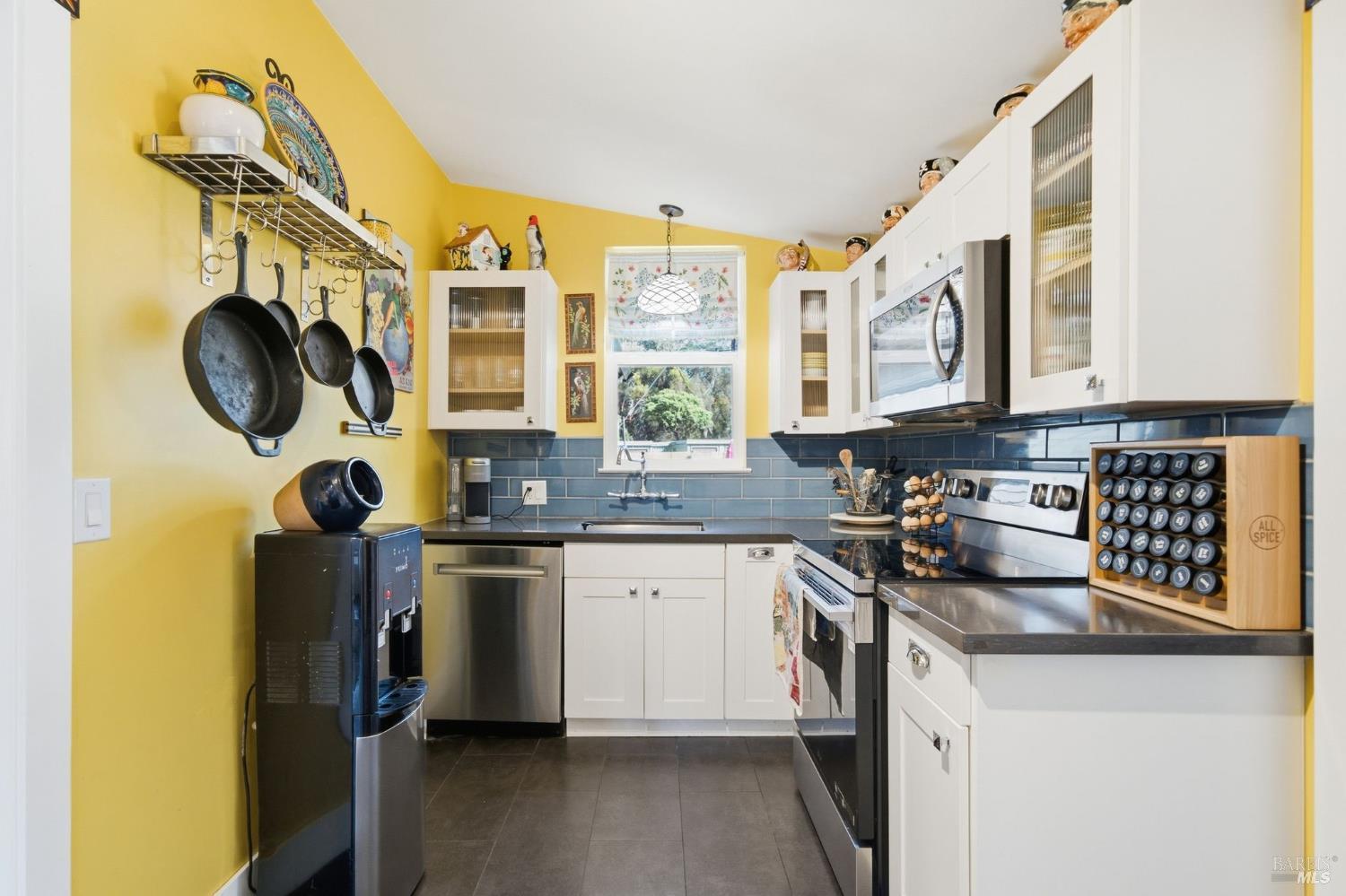 Kitchen with yellow walls, blue tile backsplash, white cabinets, and hanging pans.