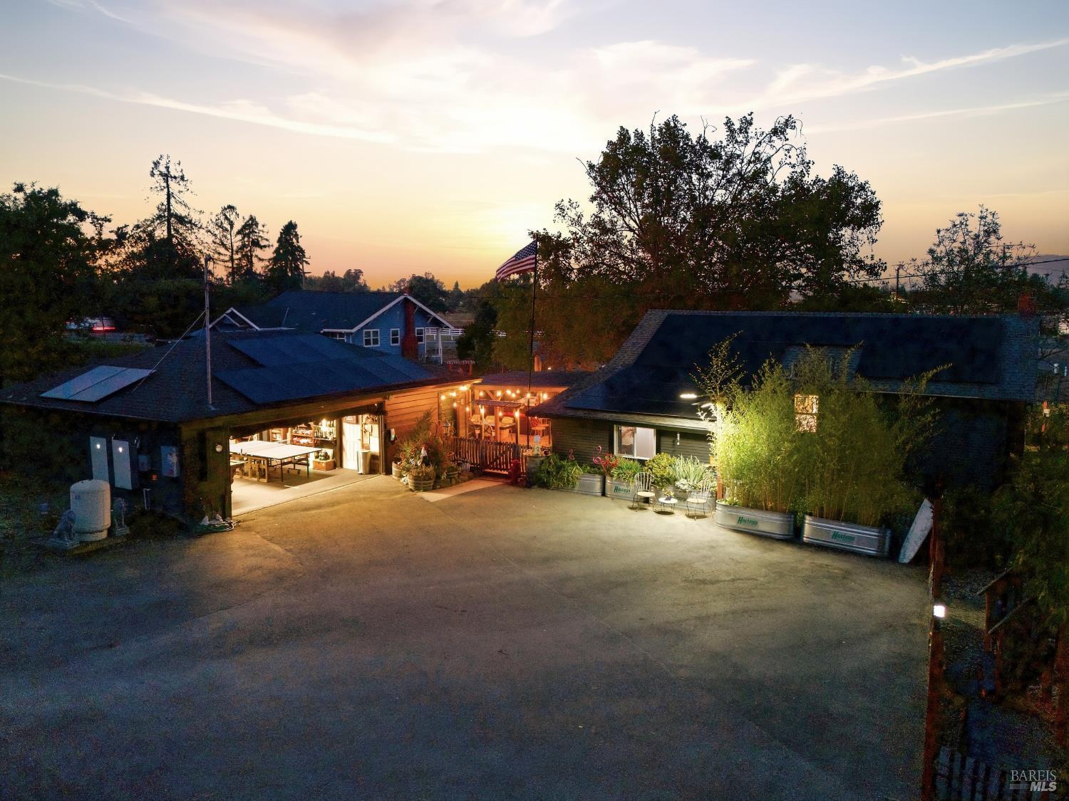 Property exterior at dusk, with an illuminated patio, broad paved area, and an American flag.