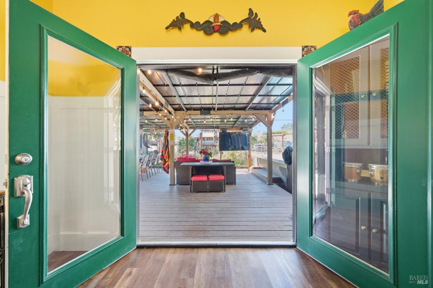 Open green doors lead from a yellow-walled room to a covered patio with seating.