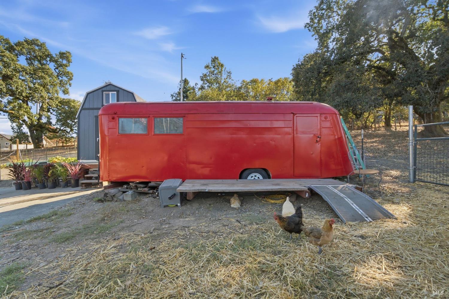 Red trailer beside a gray barn, with chickens in a straw-covered yard.