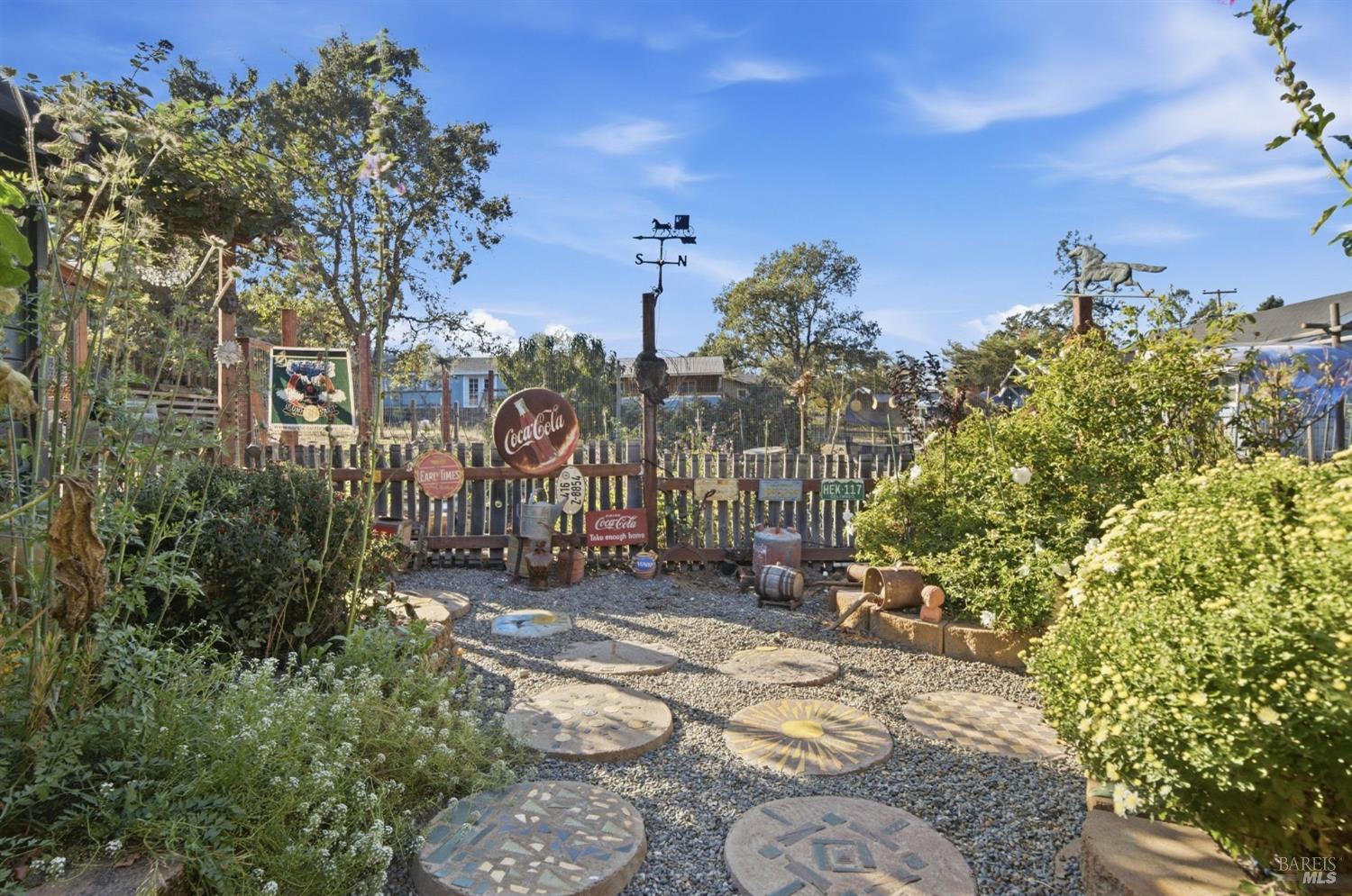 Landscaped gravel garden with mosaic stepping stones, a rustic fence, and vintage Coca-Cola signs.