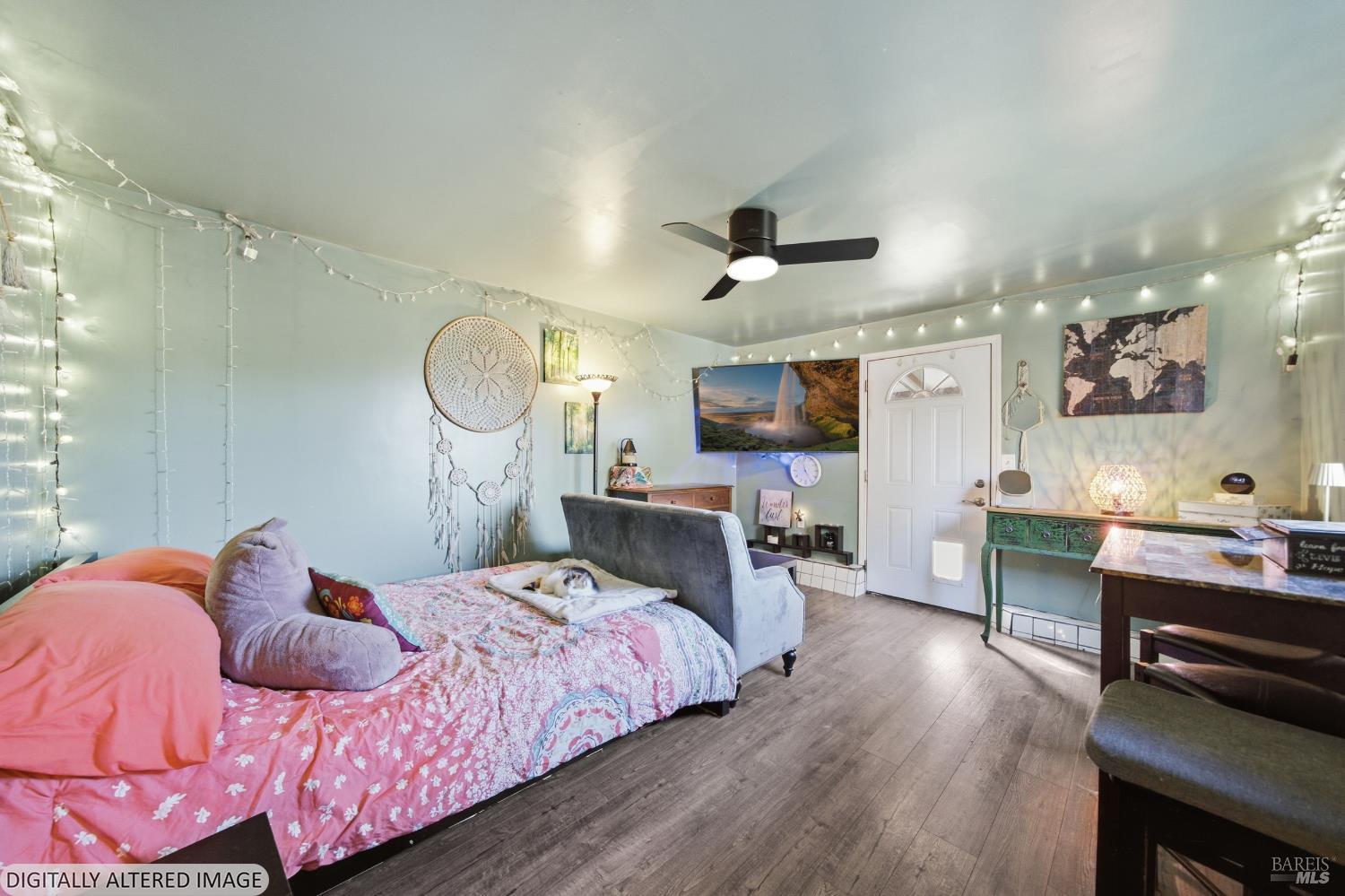 Bedroom with a pink floral bedspread, gray armchair, string lights, and a ceiling fan.