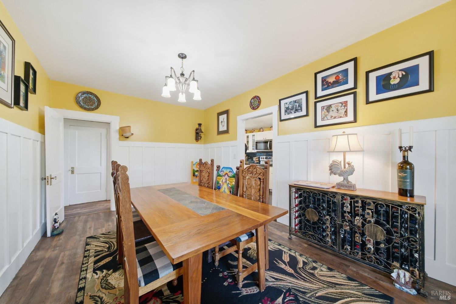Dining room with a large wooden table, carved chairs, yellow walls, and white wainscoting.