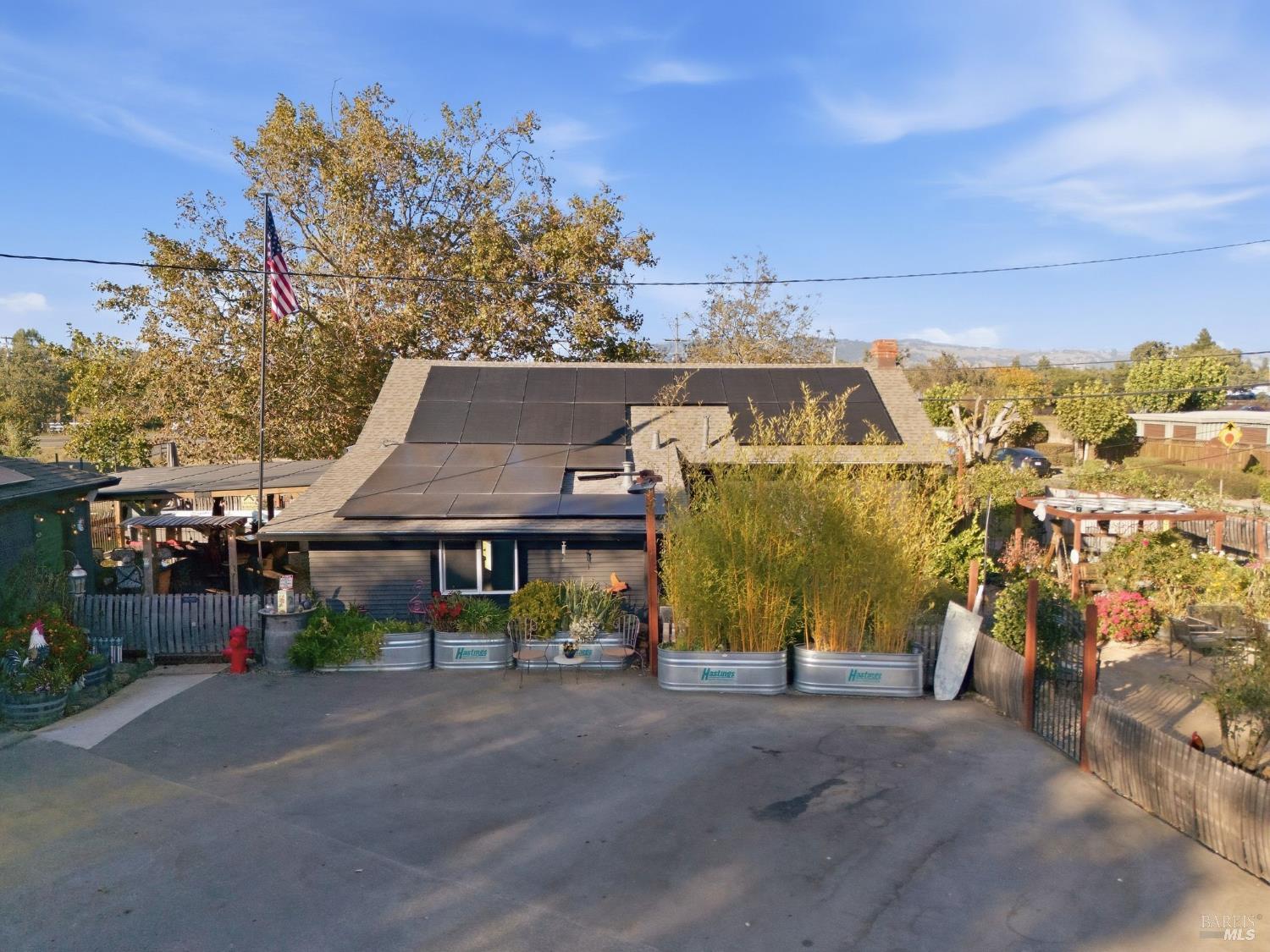 House with rooftop solar panels, raised garden beds, and patio seating beside the driveway.