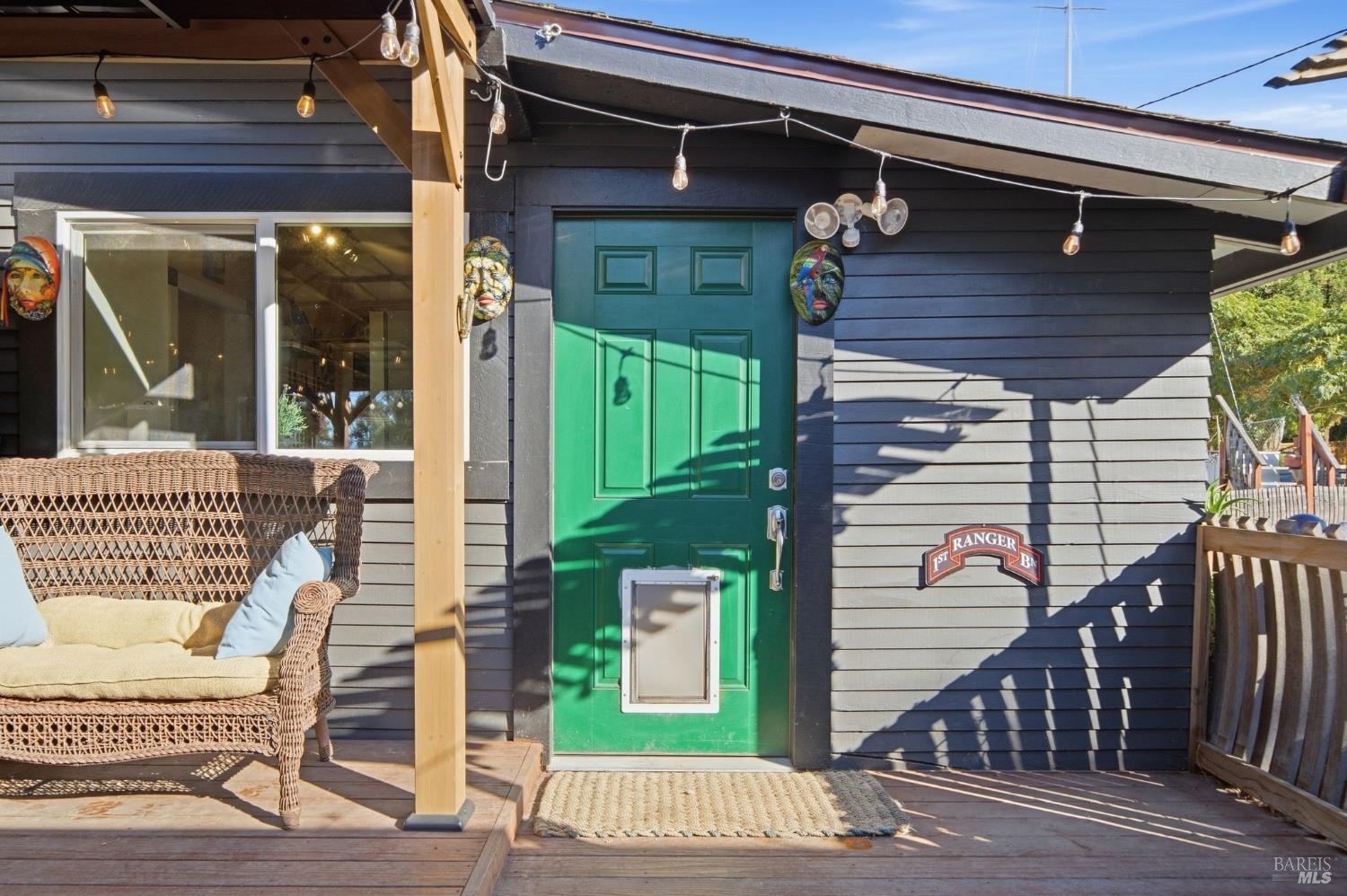 Covered porch with a green pet door, wicker seating, and string lights.