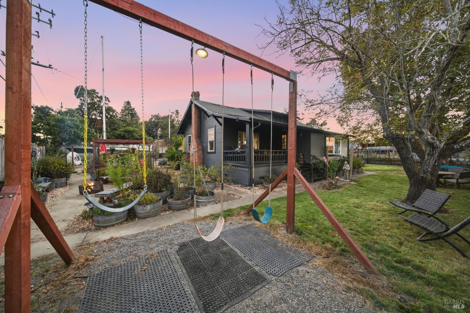 House and backyard at dusk with a large wooden swing set, raised planters, and a covered porch.