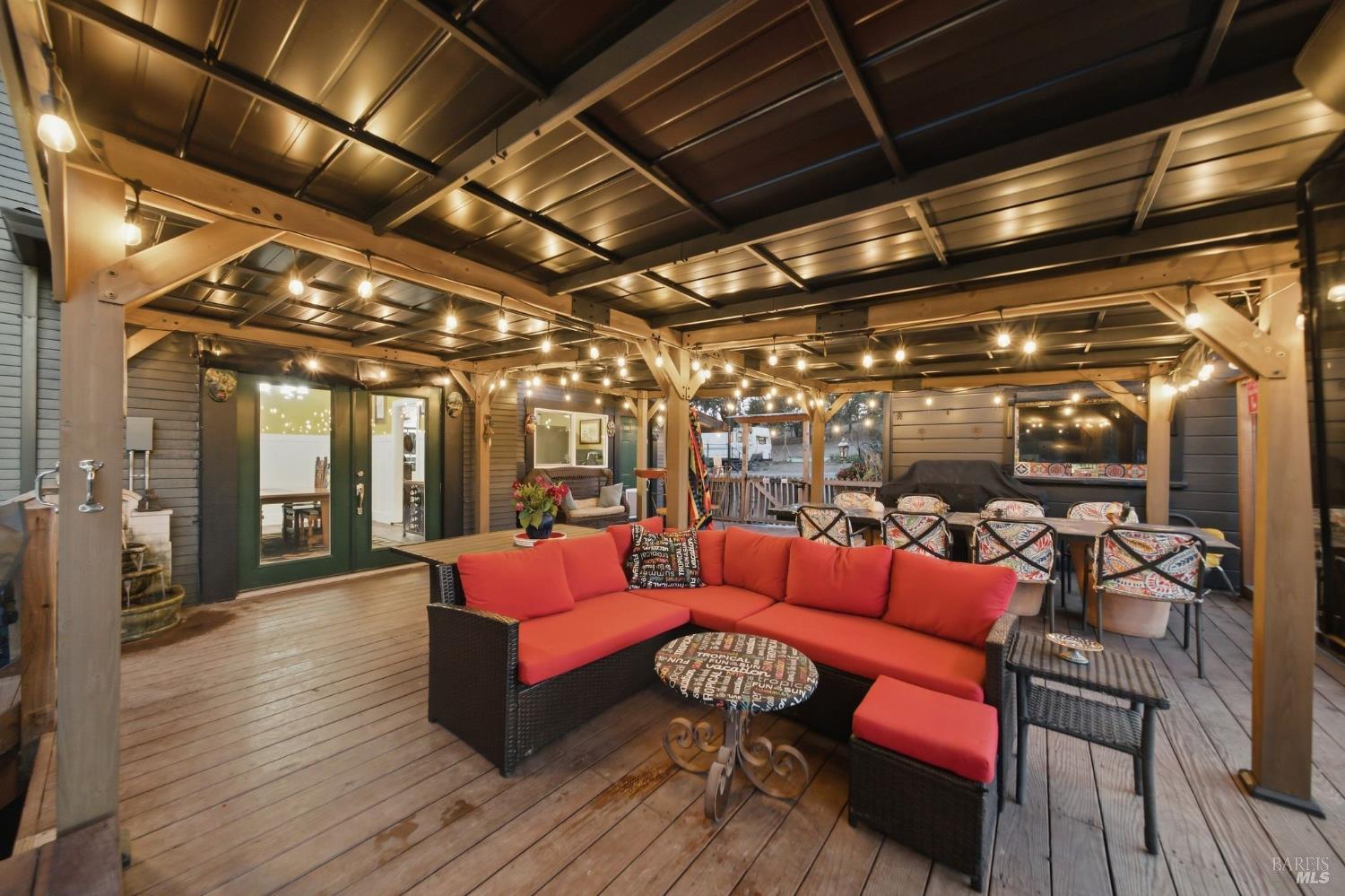 Covered patio with red sectional seating, string lights, and a dining area.