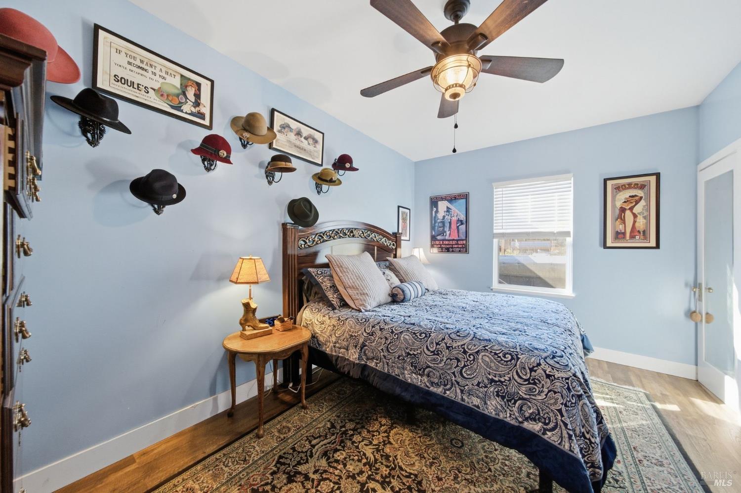 Bedroom with a carved wood bed, patterned blue bedding, and hats displayed on pale blue walls.
