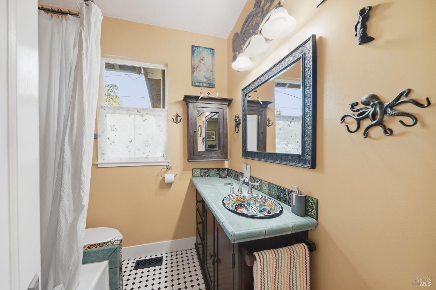 Bathroom with a colorful vessel sink, turquoise tiled vanity, and black-and-white patterned floor.