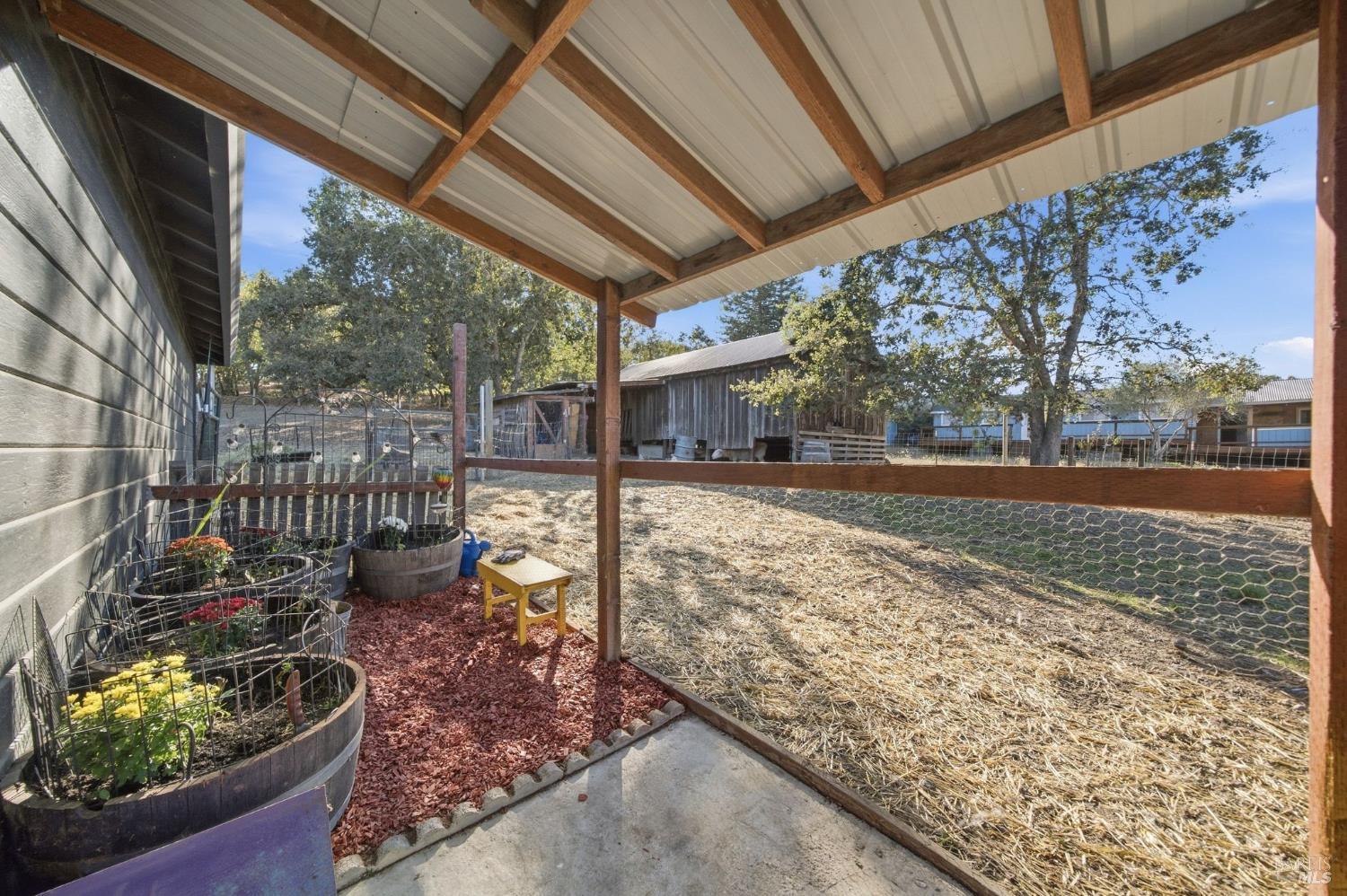 Covered patio overlooking a straw-covered fenced yard, with barrel planters and a wooden shed.