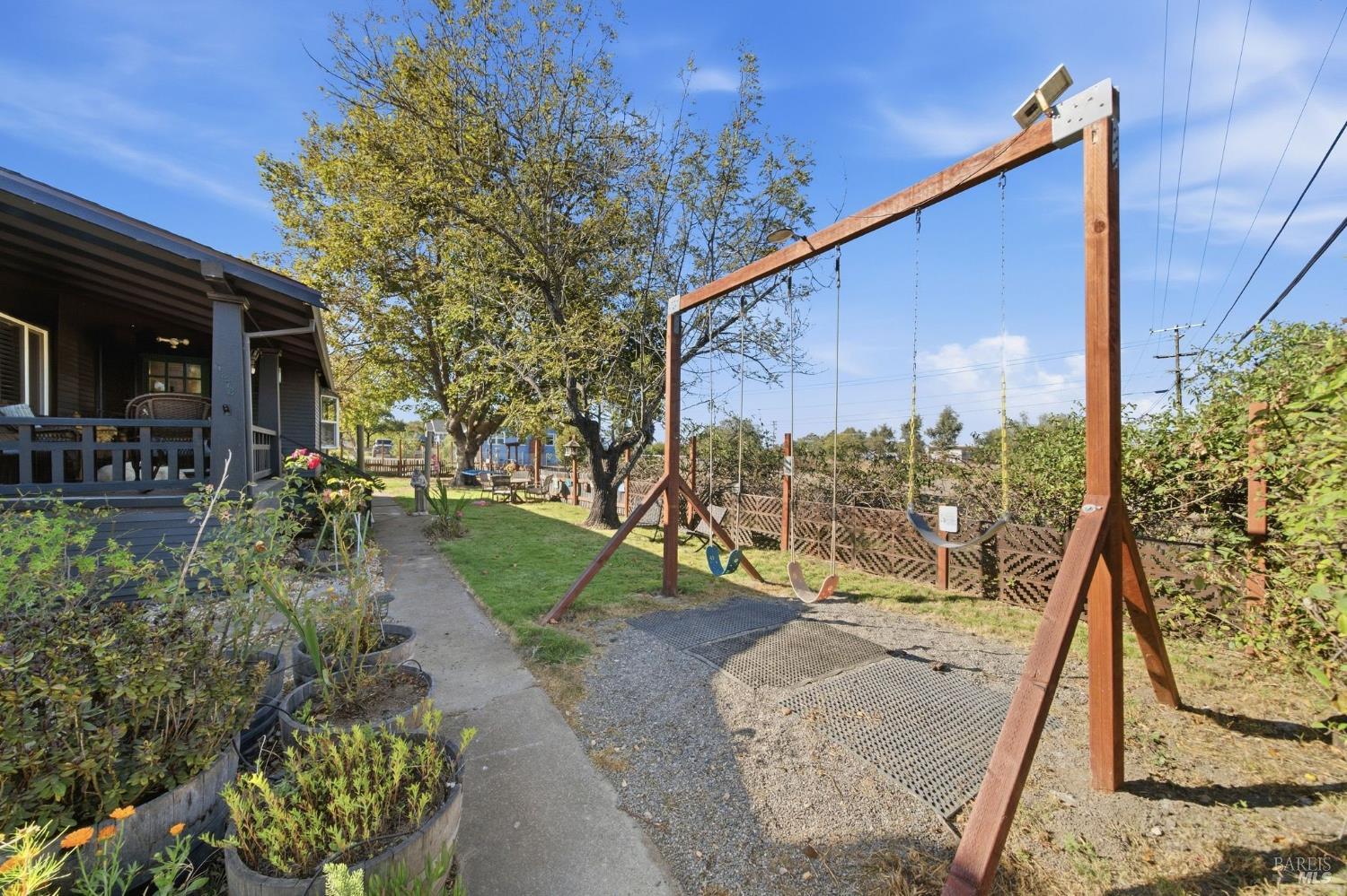 Backyard with a wooden swing set, mature tree, raised flower beds, and covered porch.