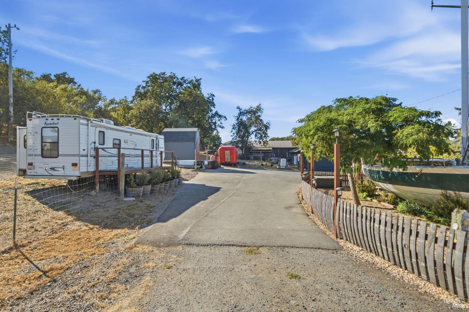 Property driveway lined with trailers and outbuildings, with a boat behind the fence.