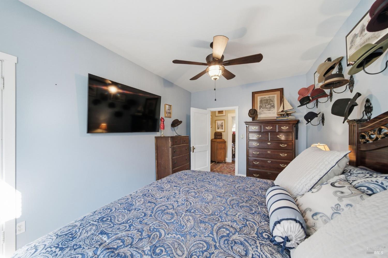 Bedroom with blue paisley bedding, dark wood dressers, and a ceiling fan.