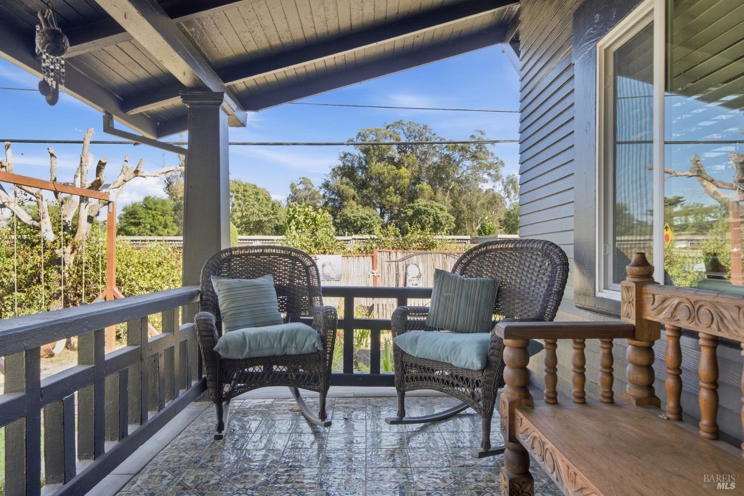 Covered porch with two wicker chairs, blue cushions, patterned tile, and a carved wooden bench.