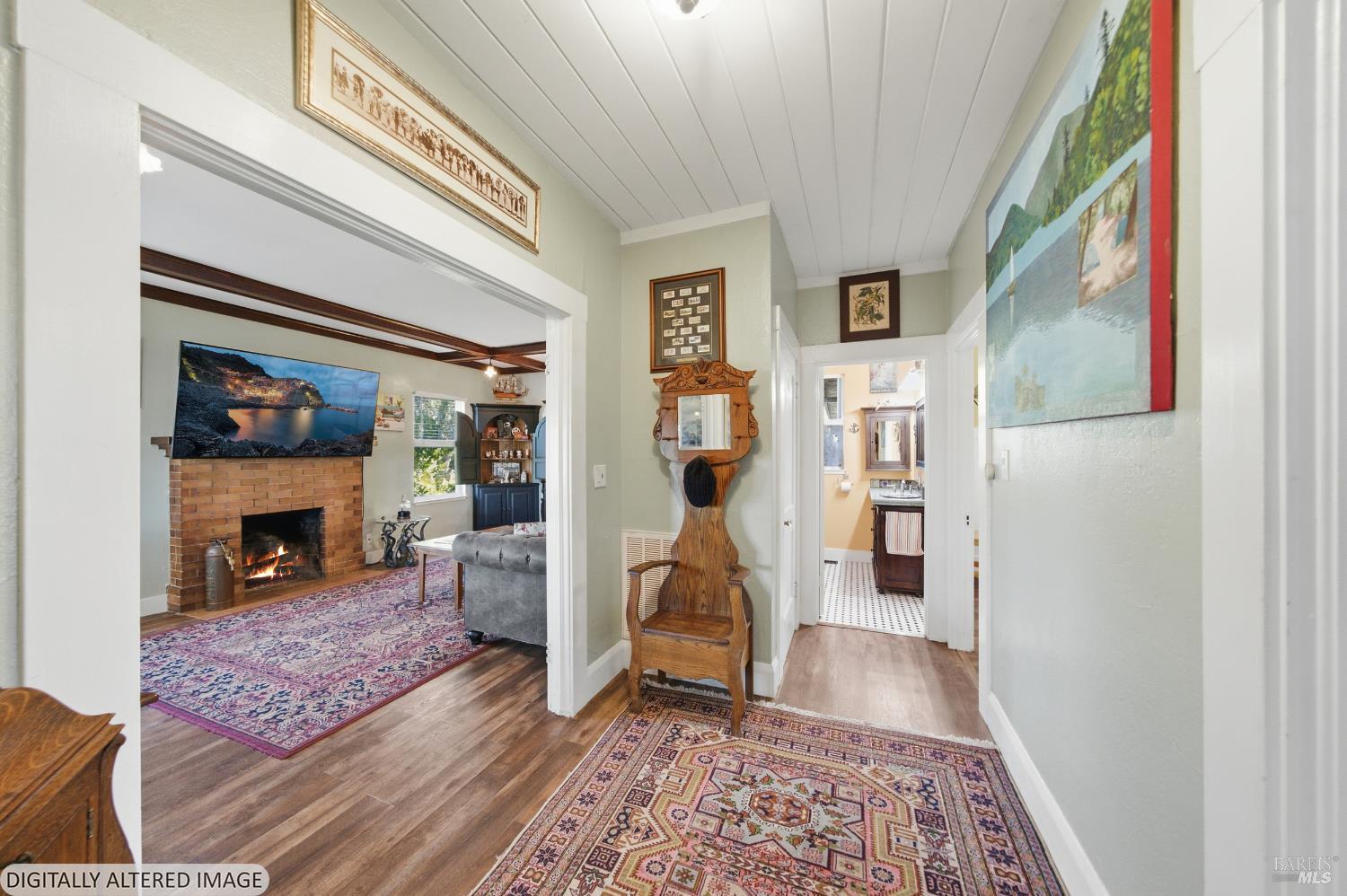 Furnished hallway with patterned rugs and antique wooden chair, opening to a living room with a brick fireplace.