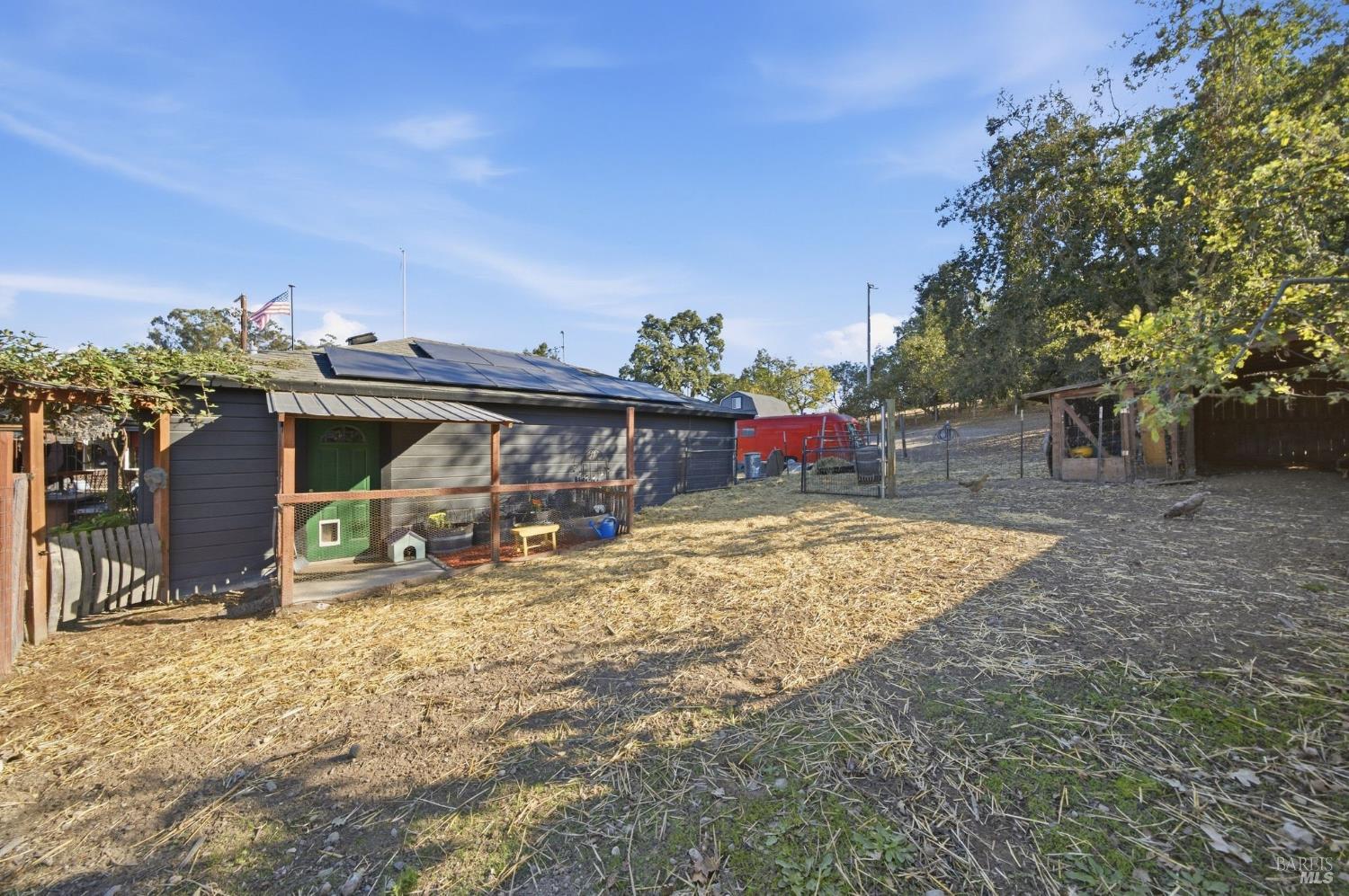 Dark-gray outbuilding with rooftop solar panels beside a dry yard and fenced animal enclosures.