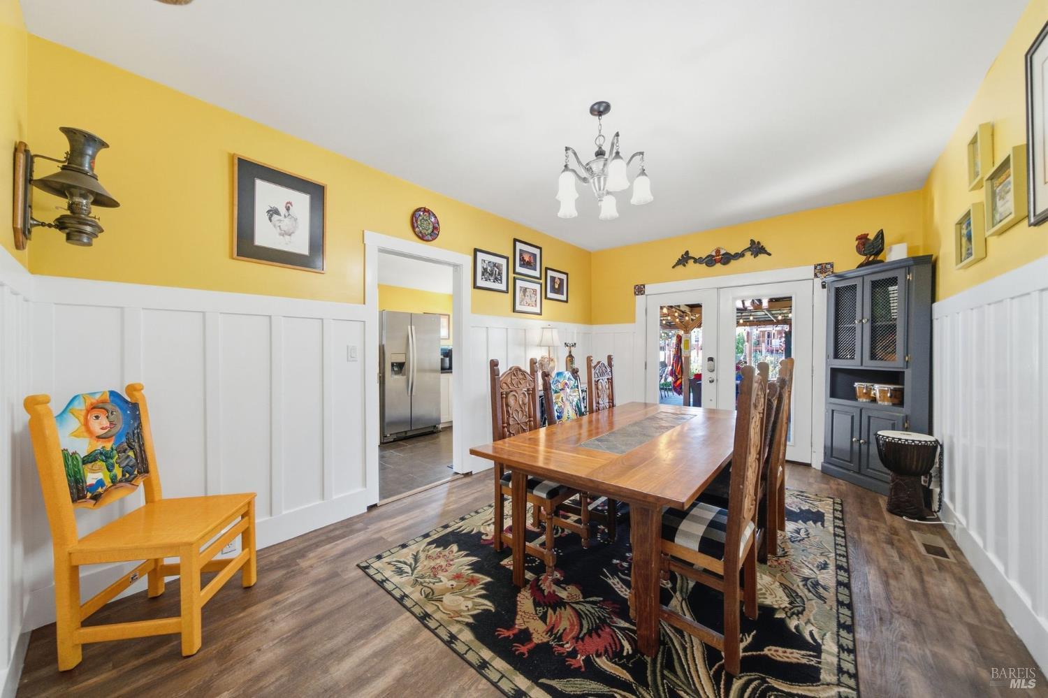 Dining room with a long wooden table, patterned rug, yellow walls, and glass doors to an outdoor area.