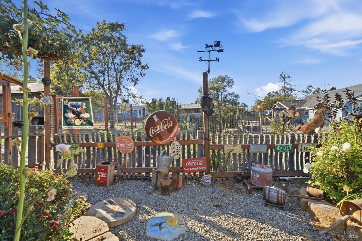 Gravel yard behind a wooden fence, decorated with vintage signs and a horse-and-carriage weather vane.