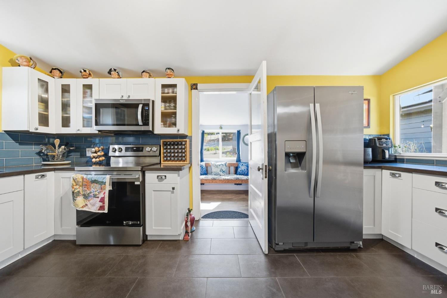 Kitchen with yellow walls, blue tile backsplash, white cabinetry, and stainless steel appliances.