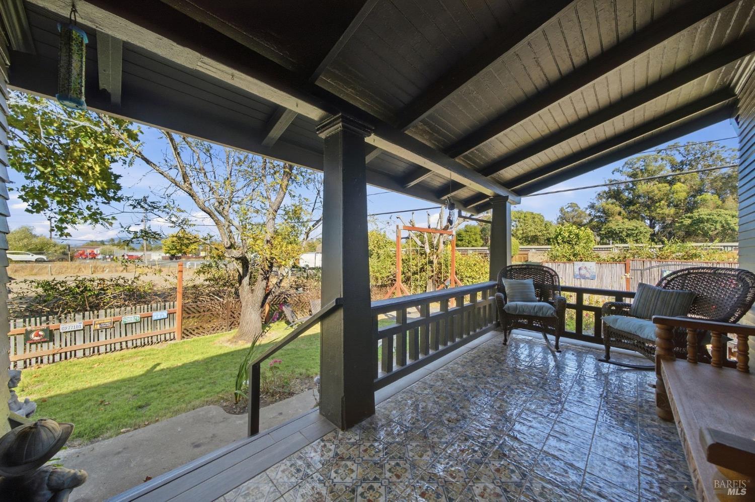 Covered patio with patterned tile flooring, wicker seating, and views of the fenced yard.