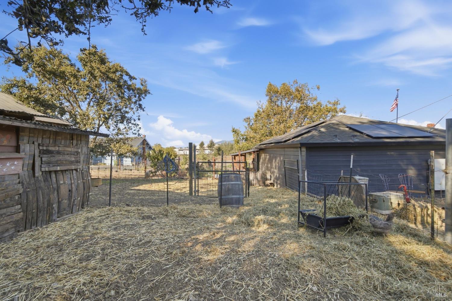 Fenced animal enclosure with straw-covered ground, rustic sheds, and solar panels on the larger shed.