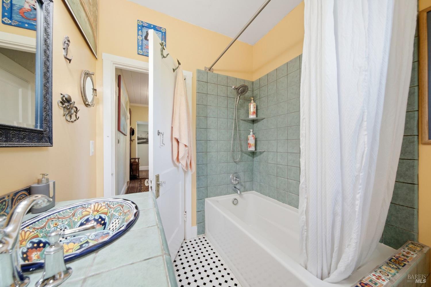 Bathroom with a tiled tub and shower, colorful vessel sink, and black-and-white geometric floor.