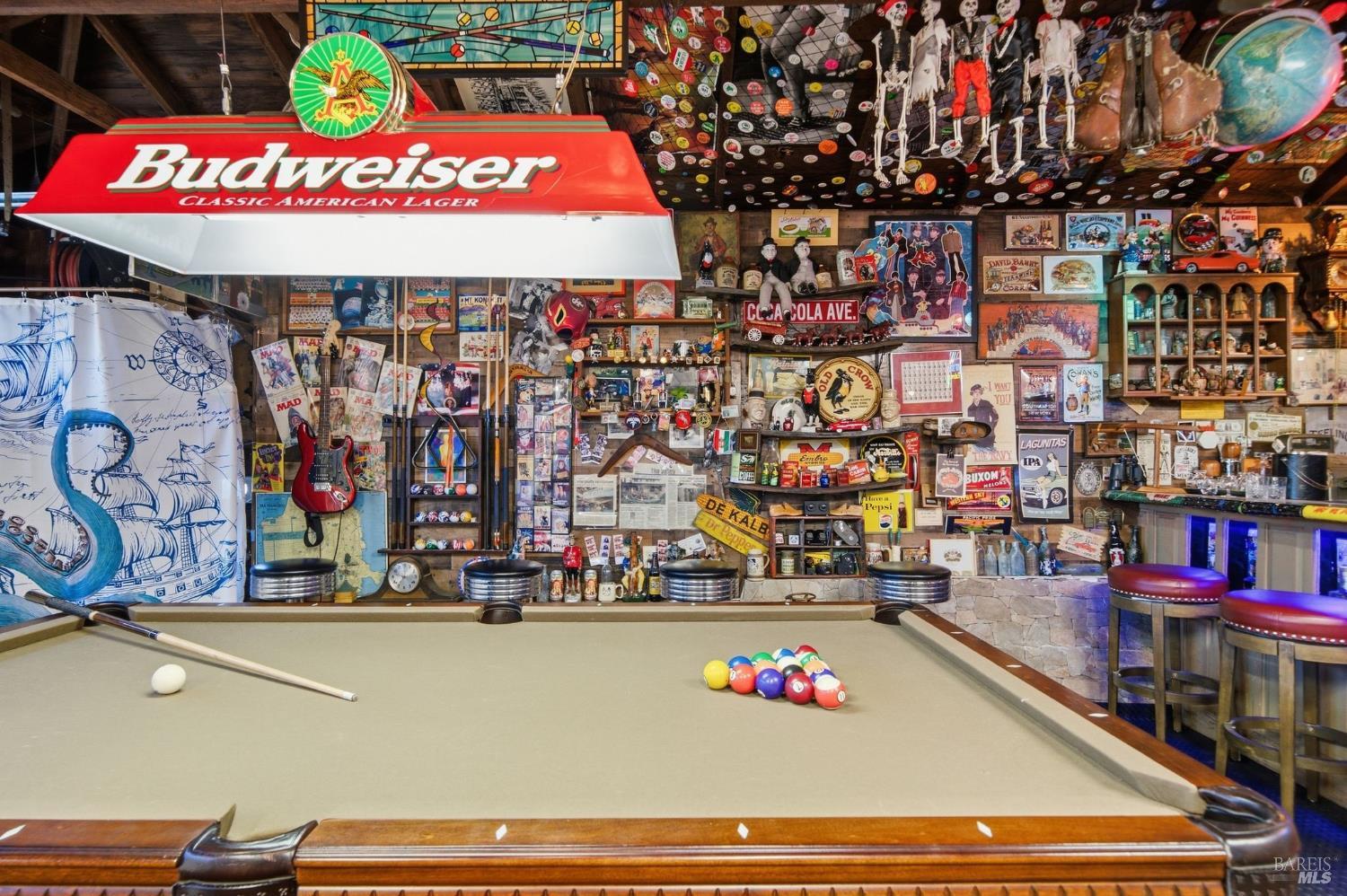 Recreation room with a billiards table, Budweiser sign, bar stools, and walls covered in vintage memorabilia.