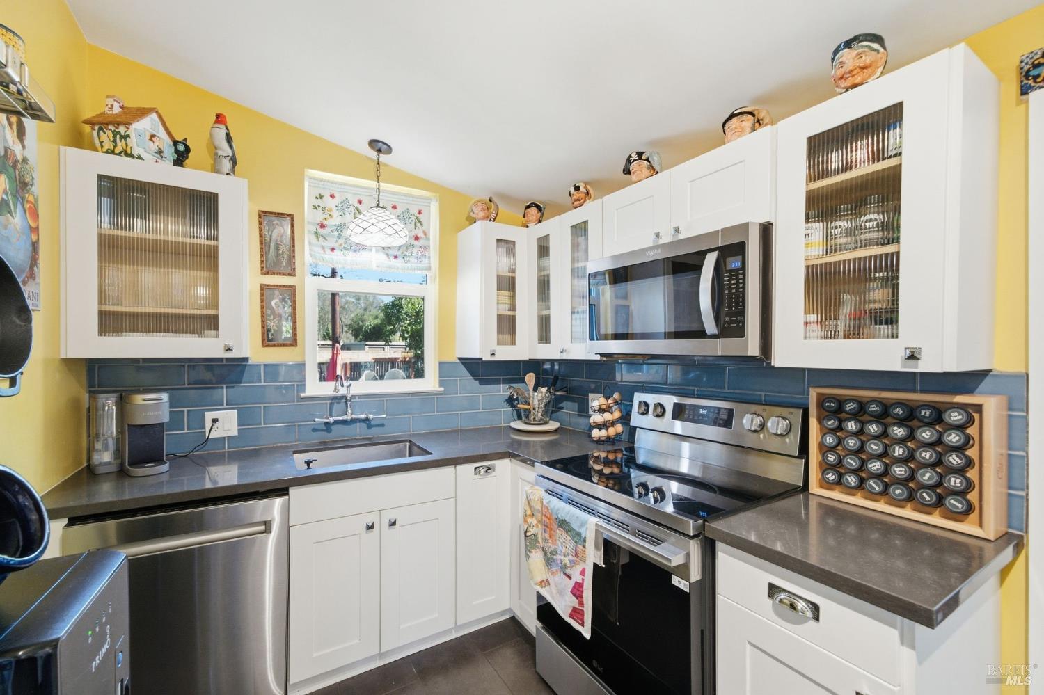 Kitchen with white cabinets, blue tile backsplash, yellow walls, and stainless steel appliances.