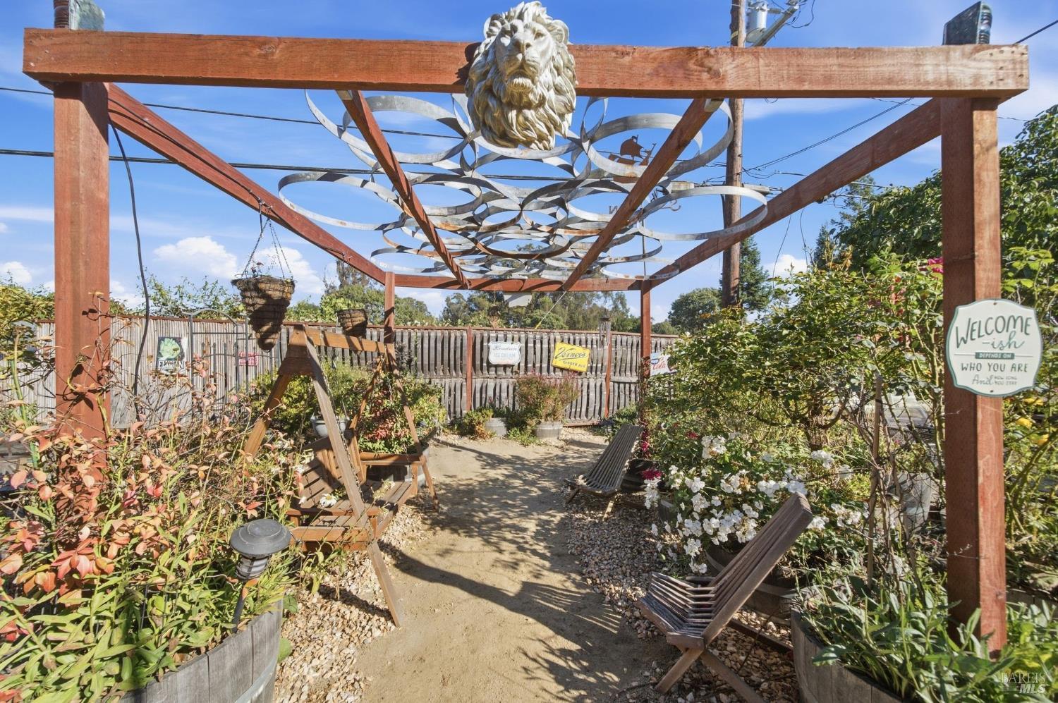 Garden seating beneath a wooden pergola with looping metalwork and a sculpted lion head.