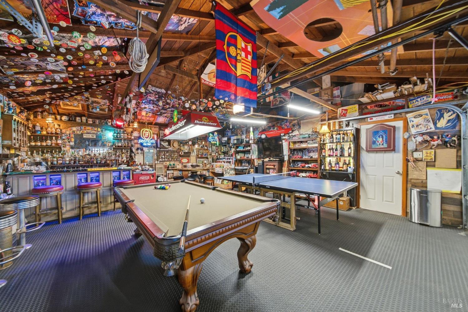 Game room with a pool table, ping-pong table, bar stools, and sports memorabilia covering the ceiling and walls.