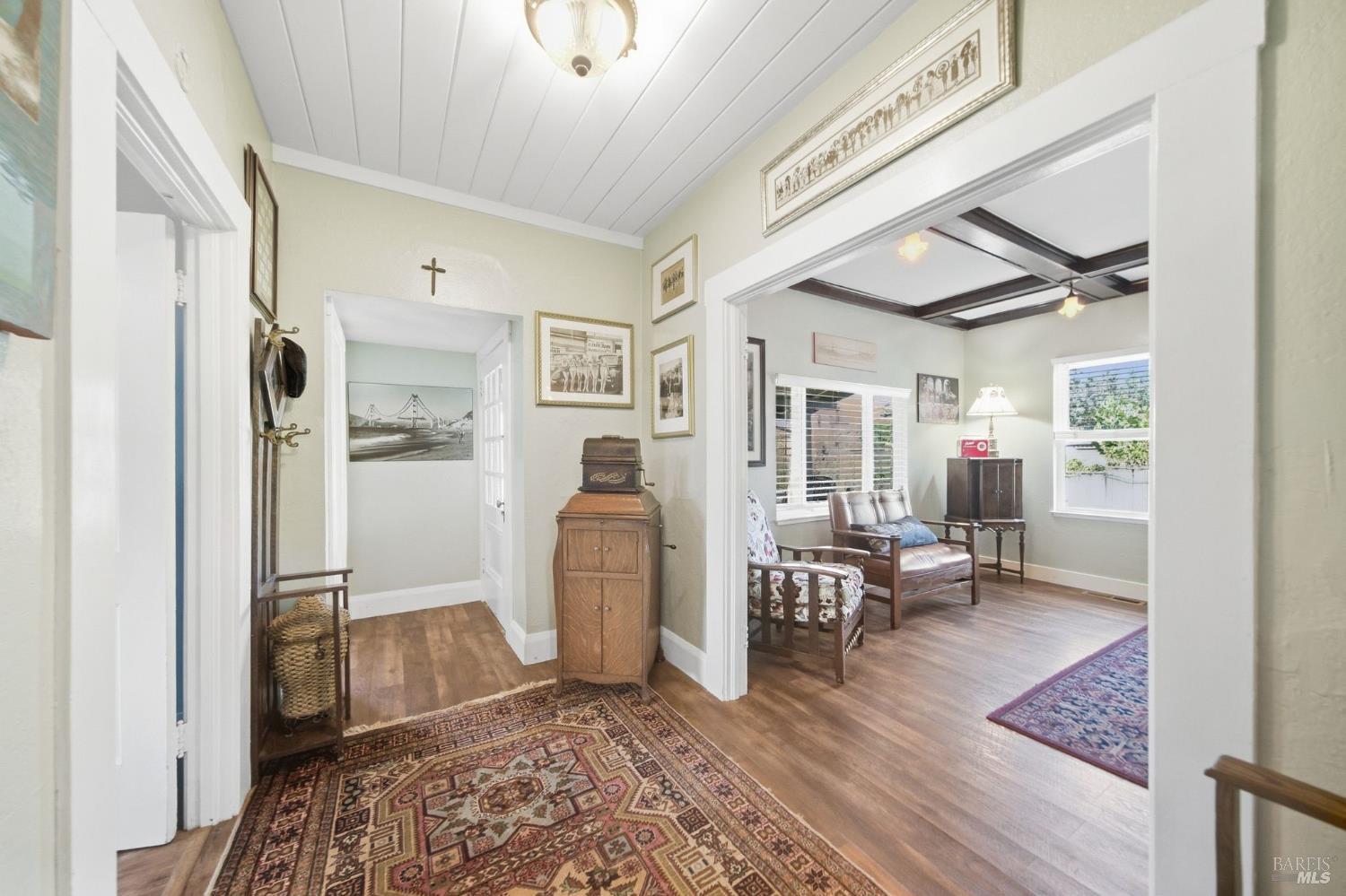 Hallway opening into a sitting room with dark ceiling beams and vintage furnishings.
