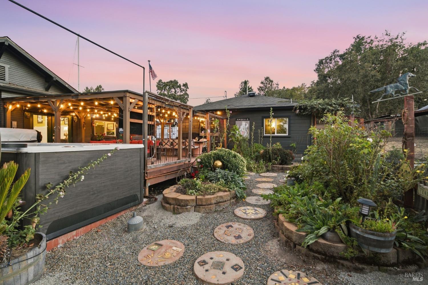 Home exterior with a string-lit covered patio, hot tub, and stepping-stone garden at dusk.