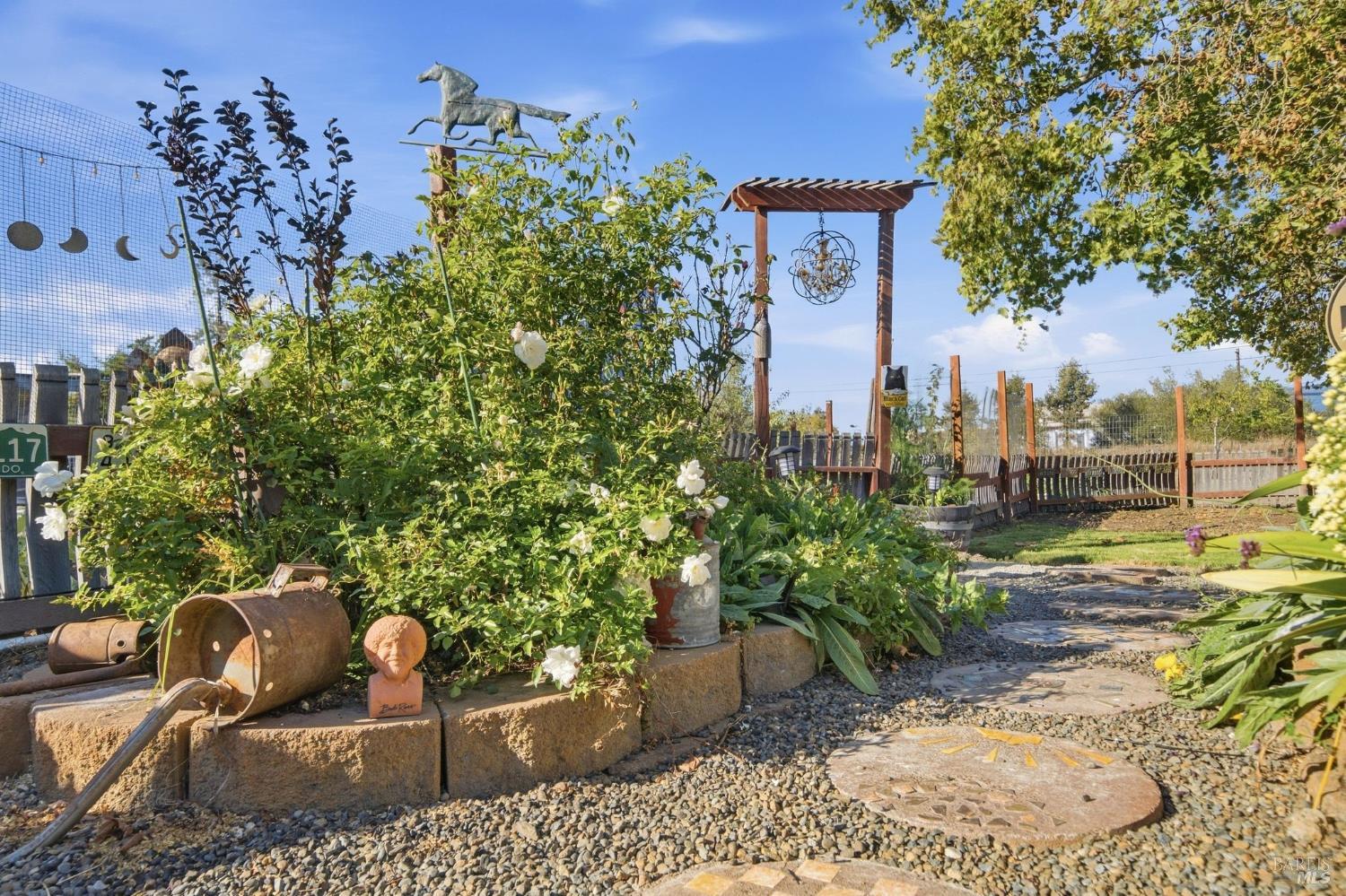 Landscaped garden with white flowers, a stone path, and a wooden arbor.