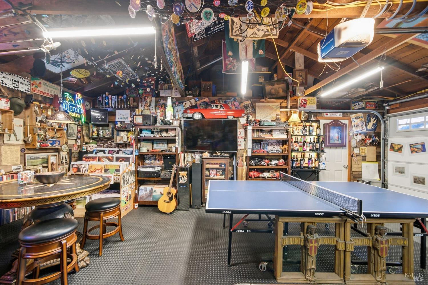 Garage game room with a ping-pong table, bar stools, collectibles, and a red model car above the television.