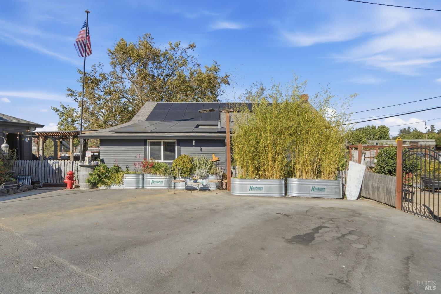 Gray single-story building with rooftop solar panels, bamboo planters, a paved forecourt, and an American flag.