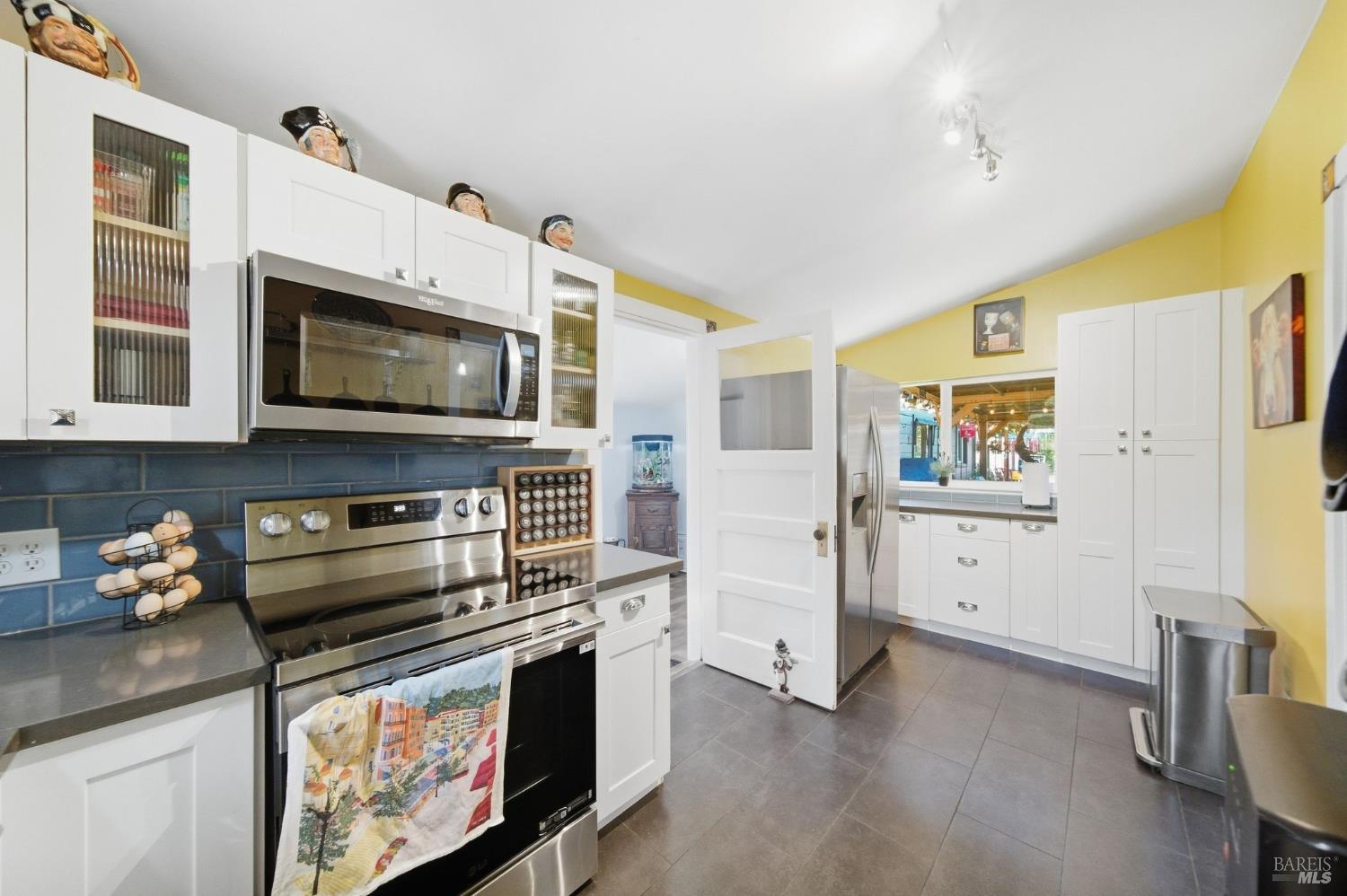 Kitchen with white cabinets, stainless steel appliances, and a dark blue tile backsplash.